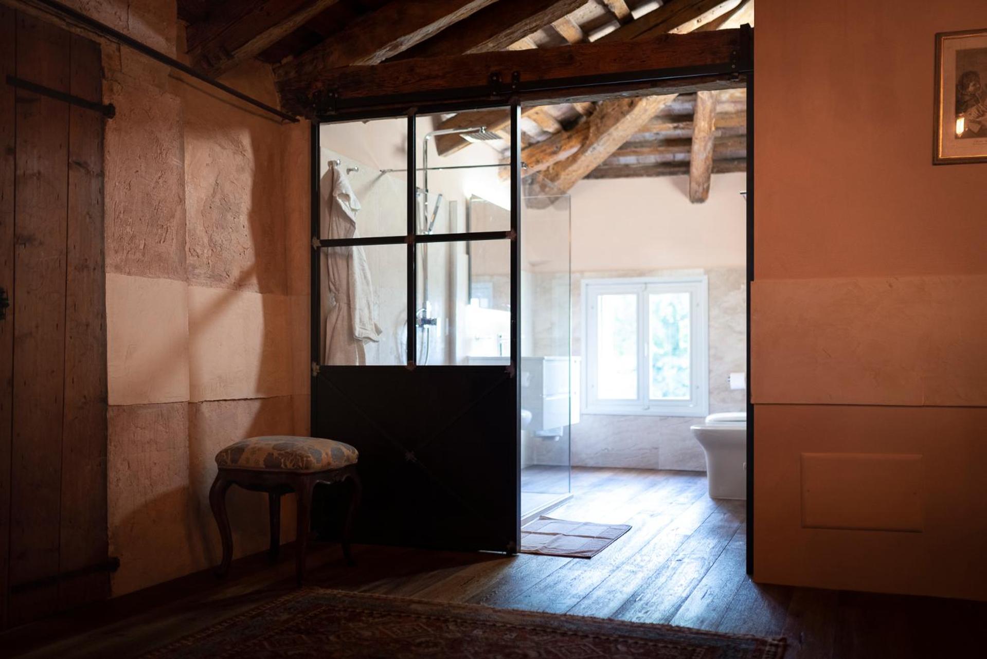 A bathroom with an exposed beam ceiling seen through a sliding black-framed glass door.
