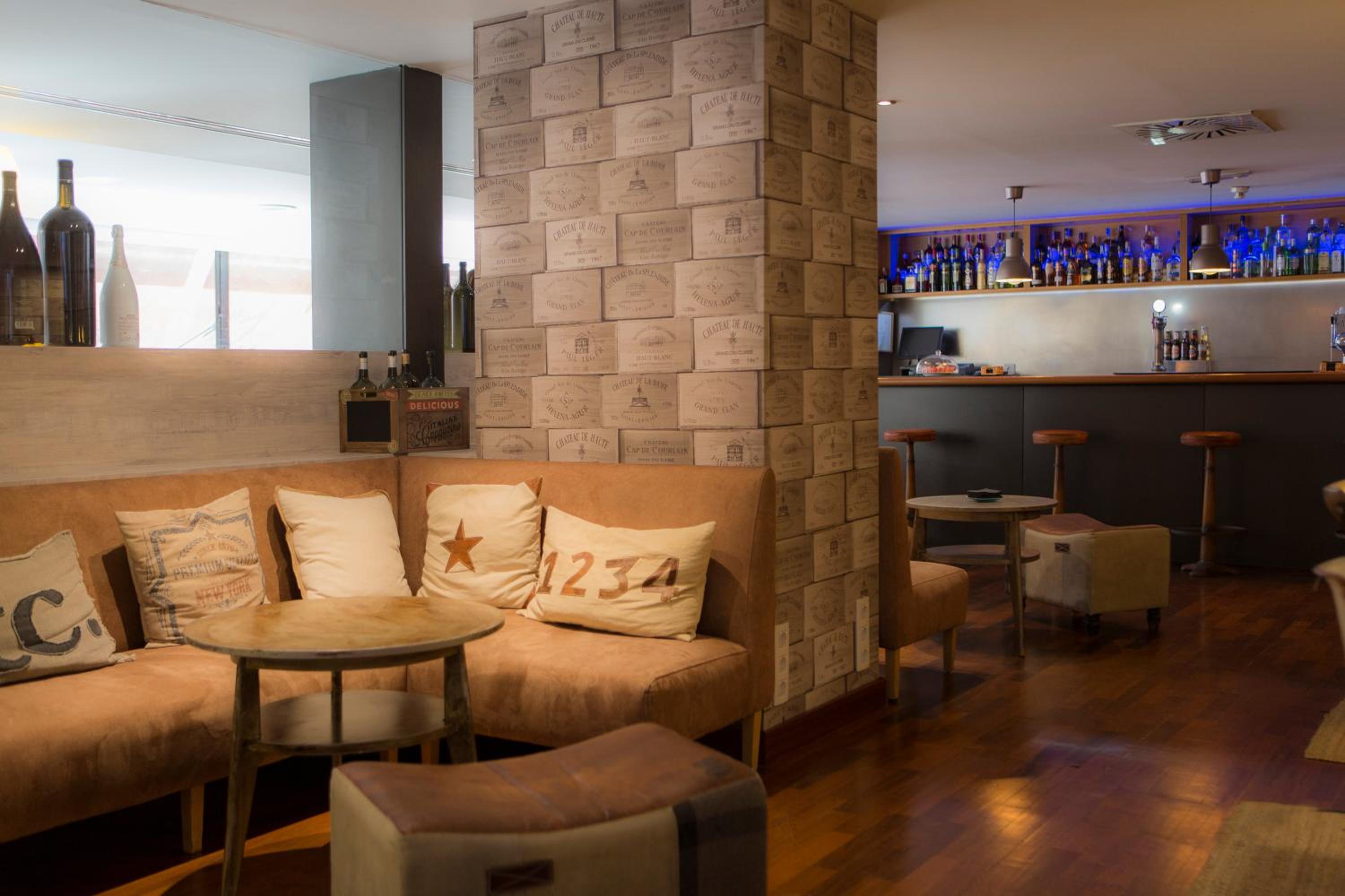 A bar seating area with upholstered sofas, small tables, and a pillar patterned with wine crate labels.