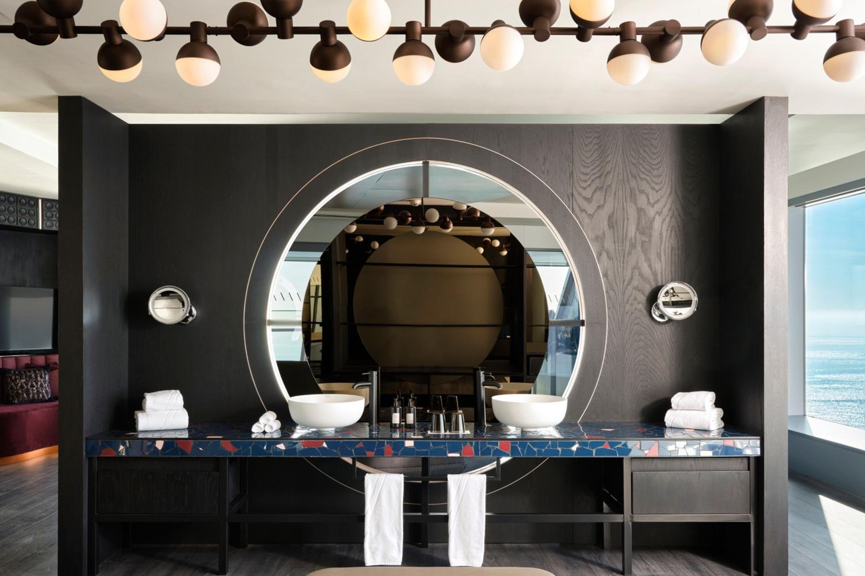 Bathroom vanity with round basins, a large circular backlit mirror, and dark wood paneling.