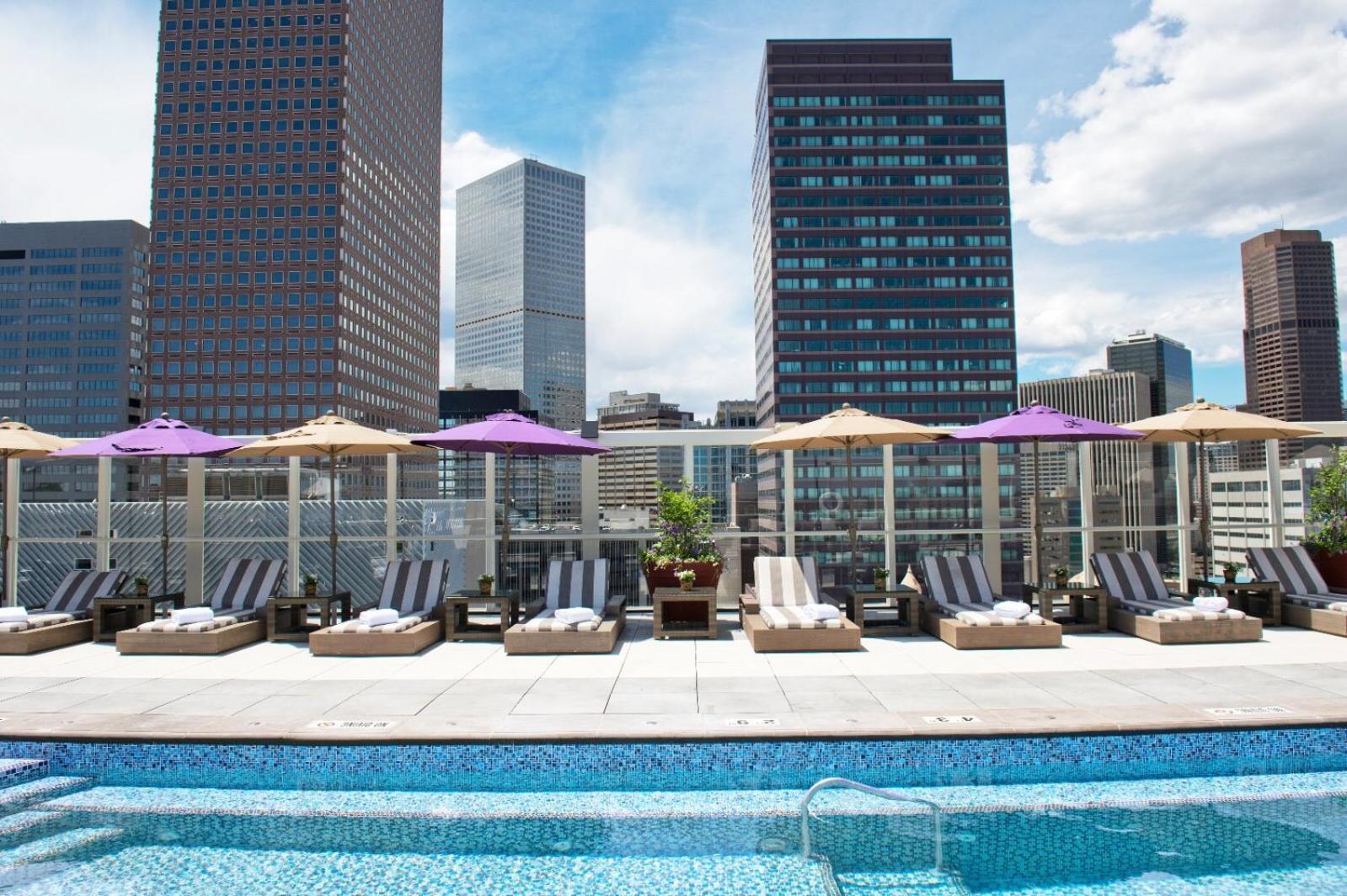 A rooftop swimming pool lined with sun loungers and umbrellas beneath downtown skyscrapers.