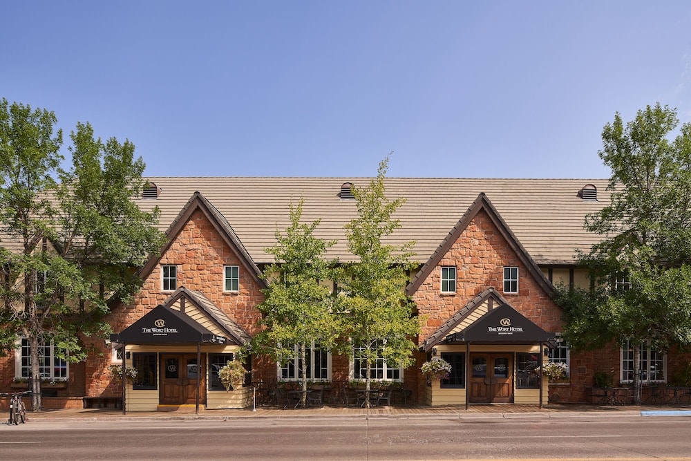 The stone facade of The Wort Hotel features gabled entrances, black awnings, and trees along the sidewalk.