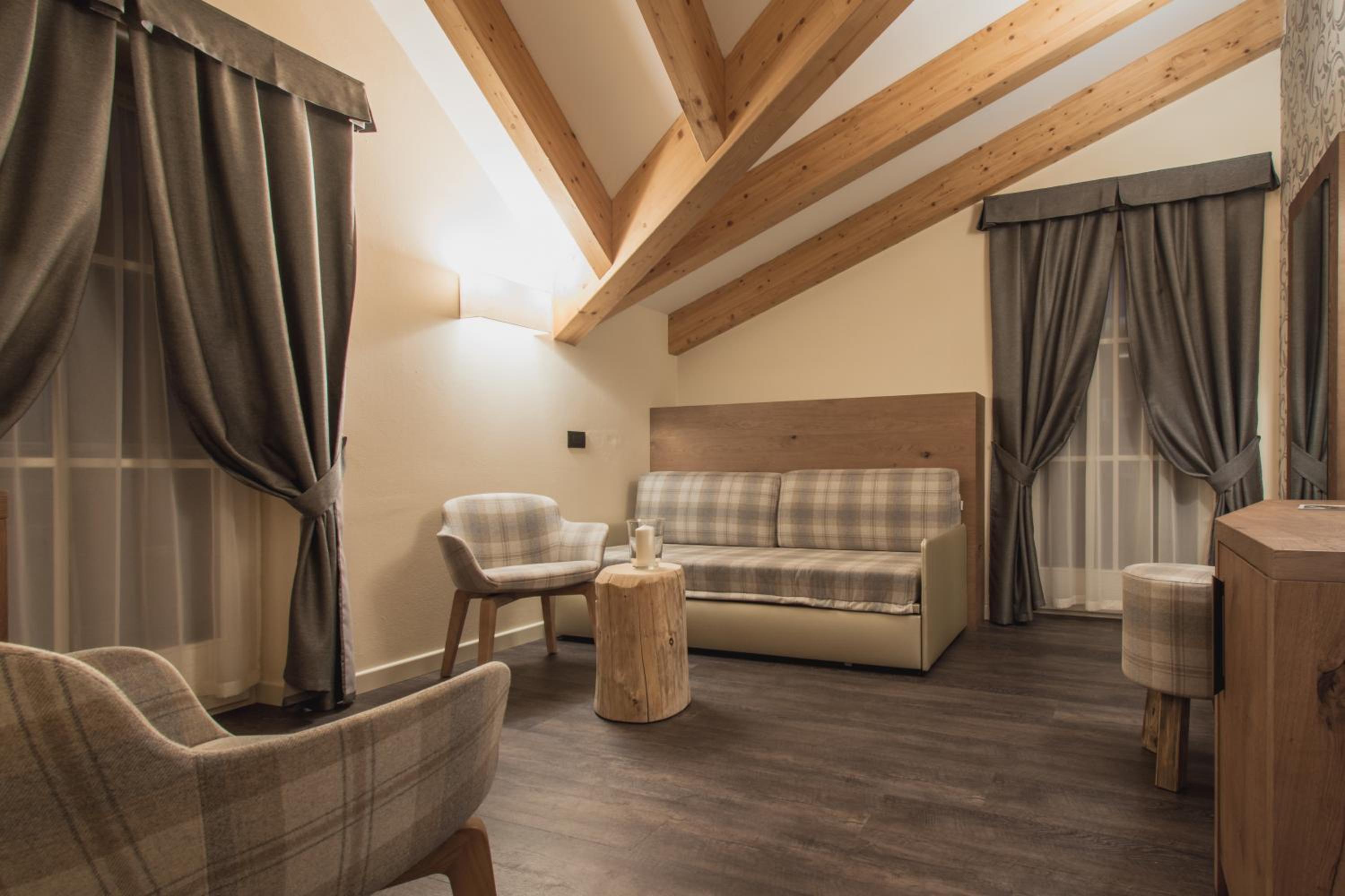 Hotel seating area featuring exposed wood ceiling beams, plaid armchairs, a matching couch, and draped windows.
