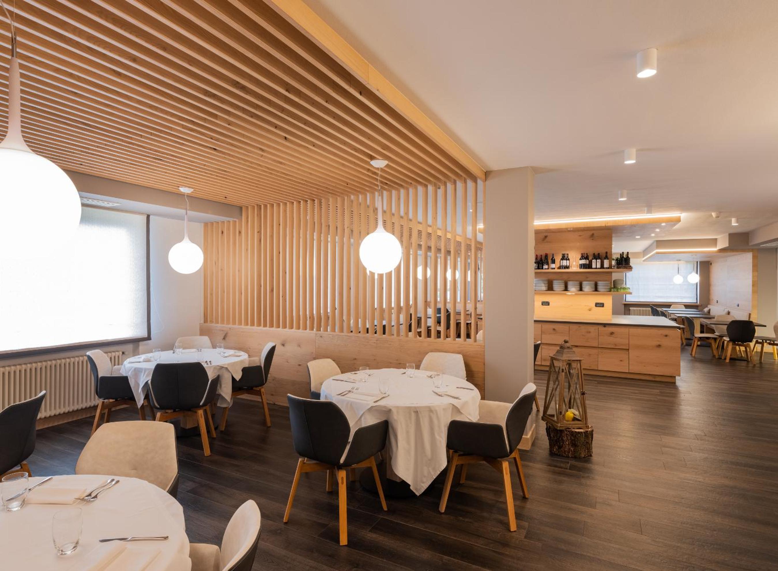Dining room with round tables, white tablecloths, dark flooring, and slatted light wood ceiling features.