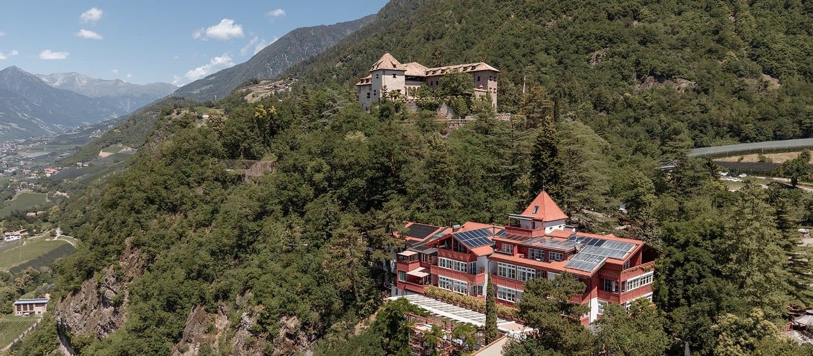 Castel Fragsburg on its wooded ridge above Merano, the red villa below and the mountains of South Tyrol behind