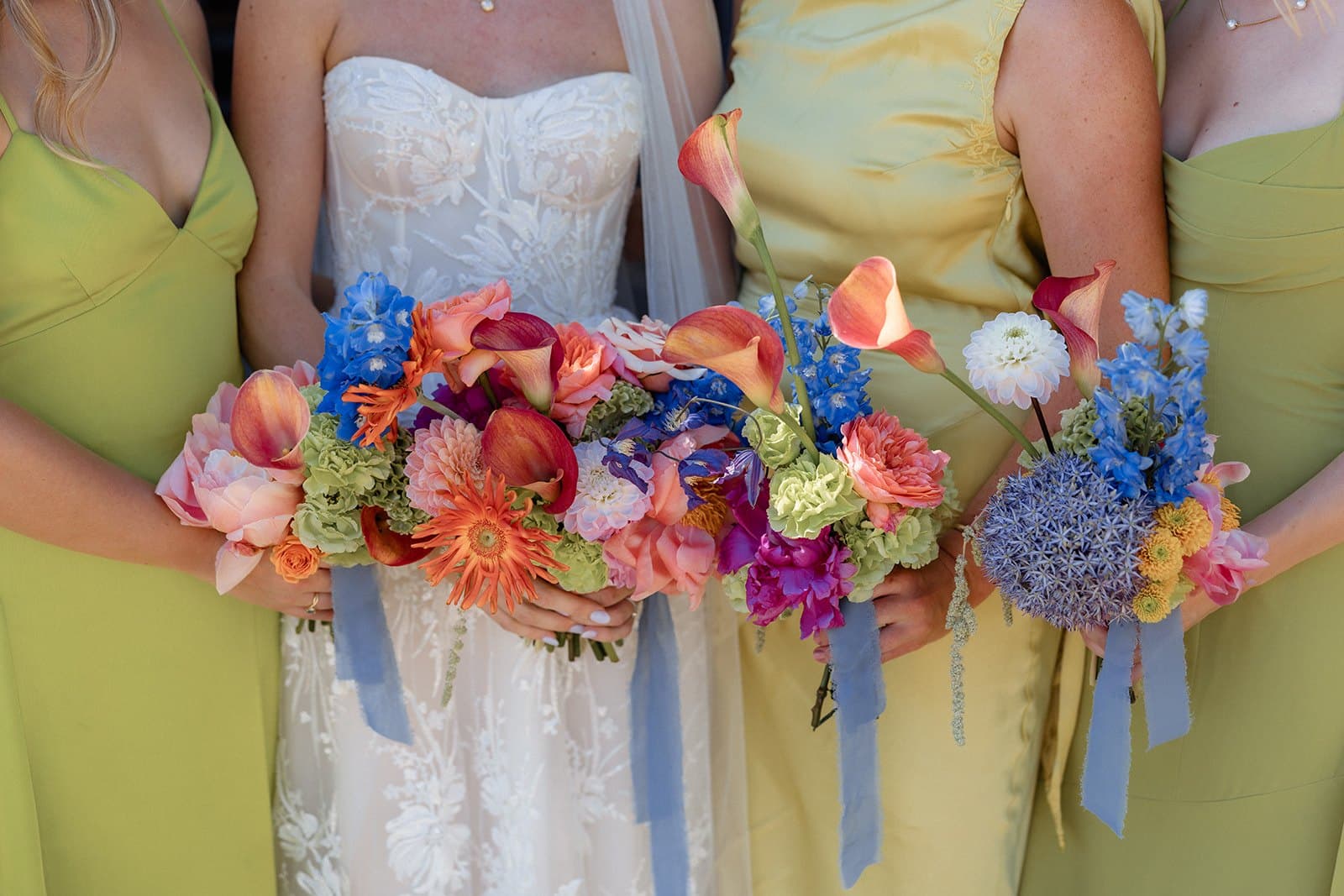 Bright bouquets of orange, pink and blue flowers held against chartreuse bridesmaid dresses