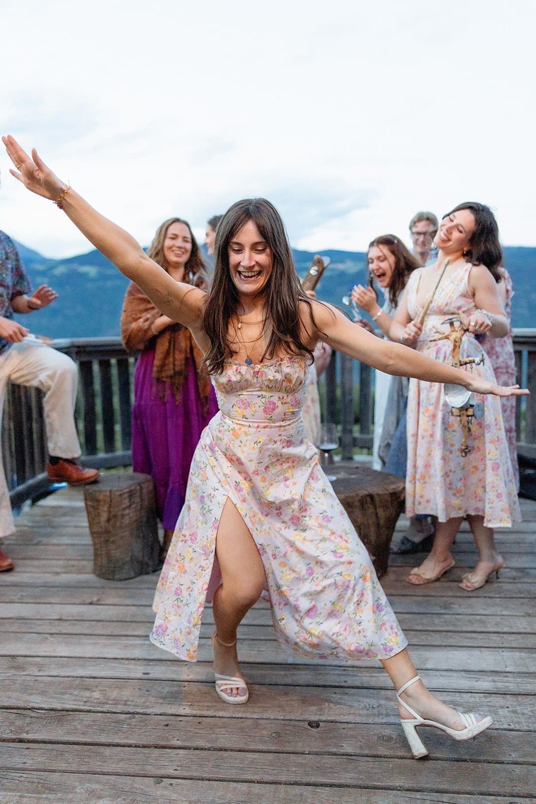 A guest in a floral dress dancing on a wooden deck at the welcome party, the mountains behind her