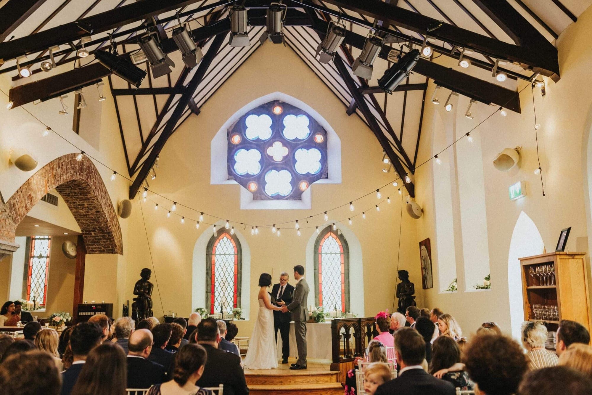 Wedding ceremony taking place indoors with a couple at the altar and guests watching.
