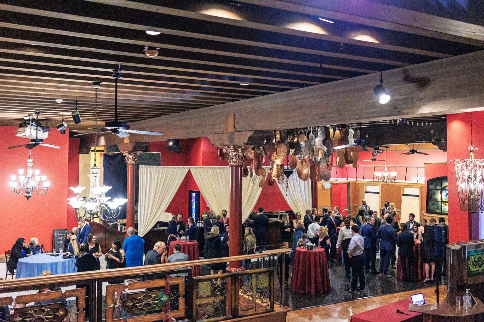 A reception hall with guests, tables, and chandeliers.