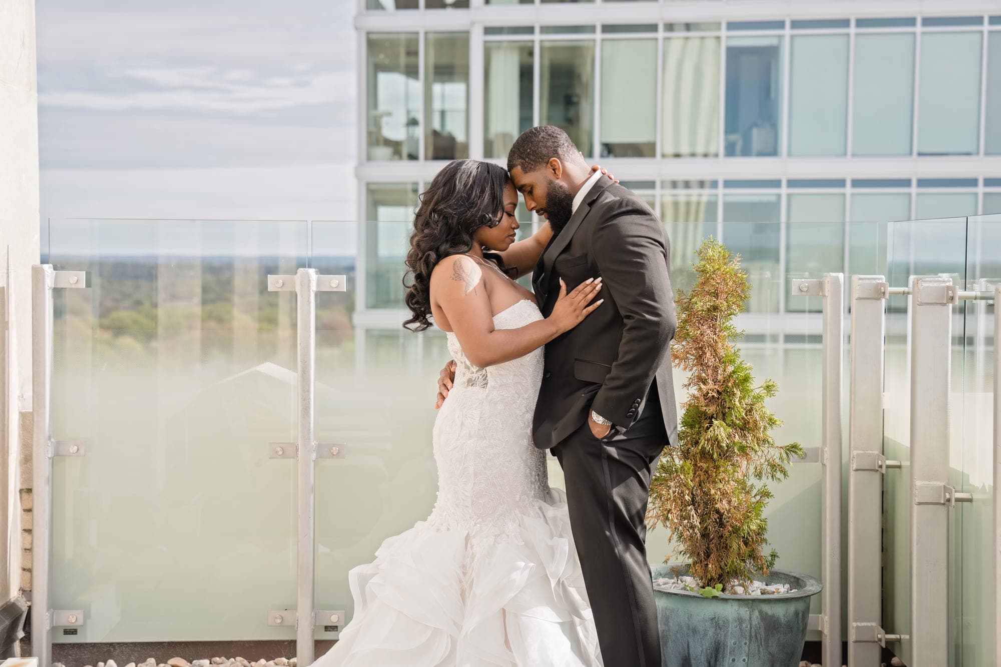 A bride and groom embrace on a balcony with a modern building behind them.