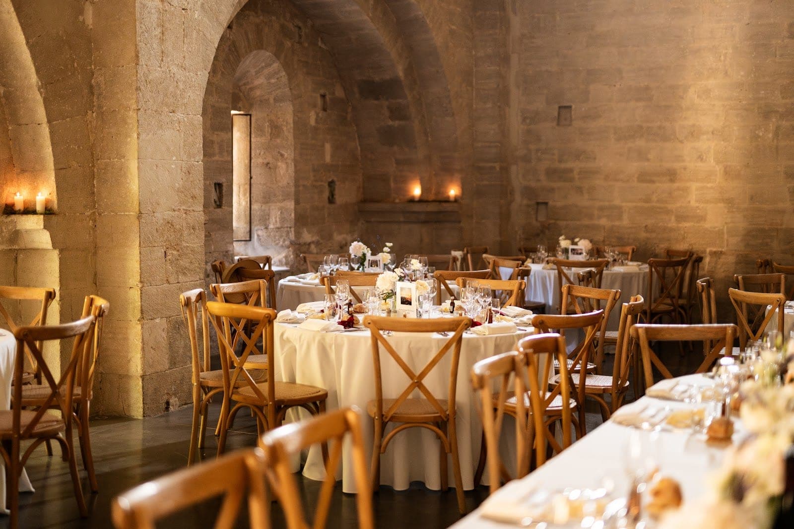 A reception hall with stone walls and arched ceilings, set with round tables and wooden chairs.
