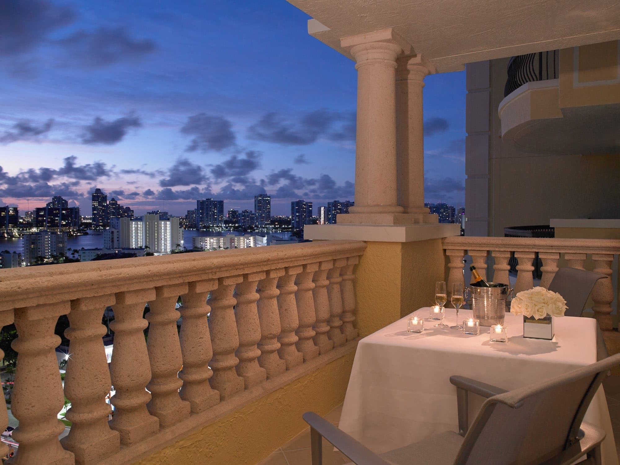 Balcony overlooking city skyline at dusk with a table set for two.