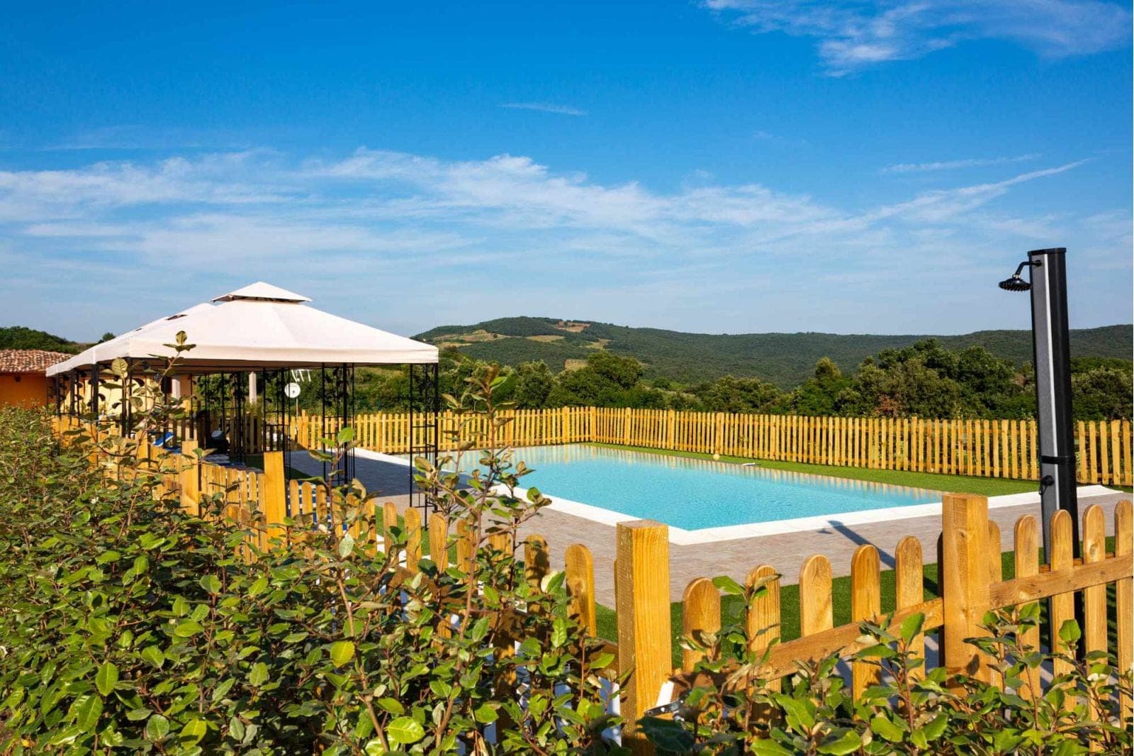 A swimming pool and gazebo are set in a garden with a view of rolling hills.