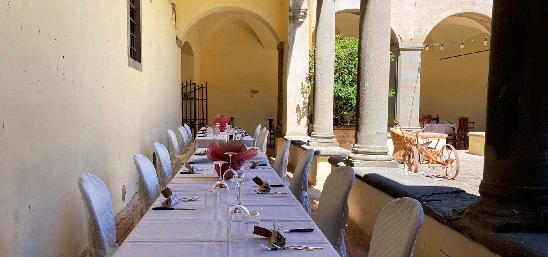 A long table set for a reception in an outdoor courtyard with chairs covered in white fabric.