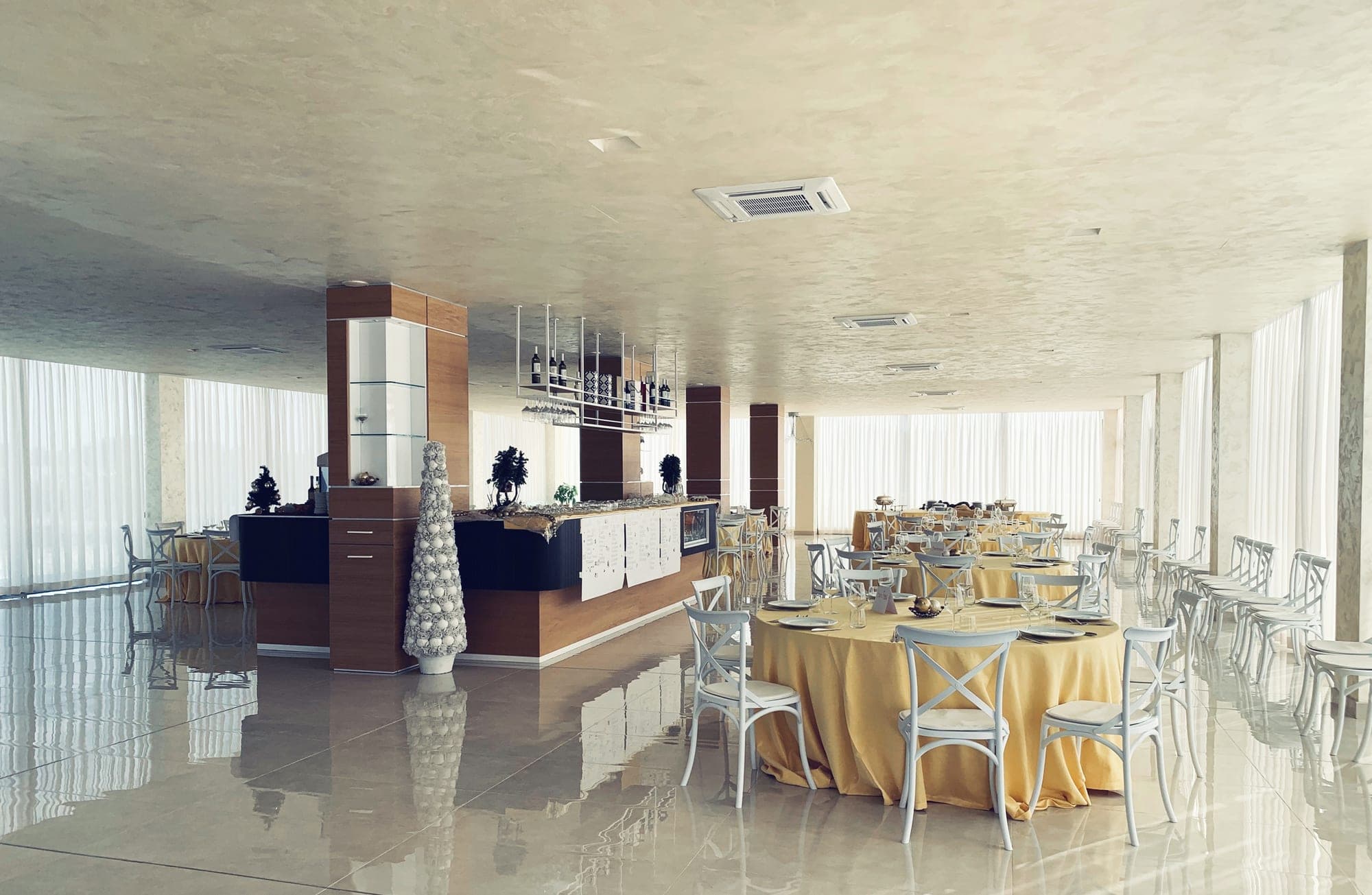 A reception room with round tables set for a wedding and a bar area.