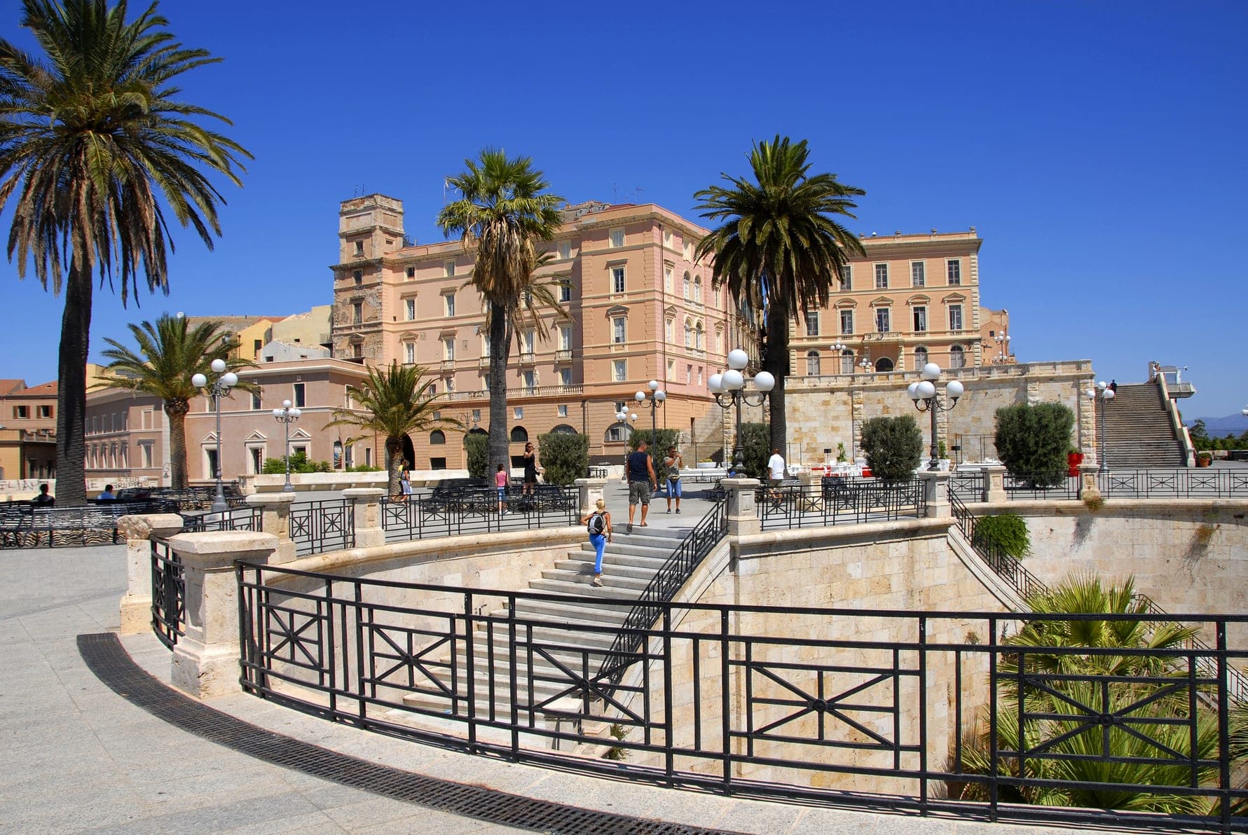Exterior view of a large, light-colored building with palm trees and a stone staircase.
