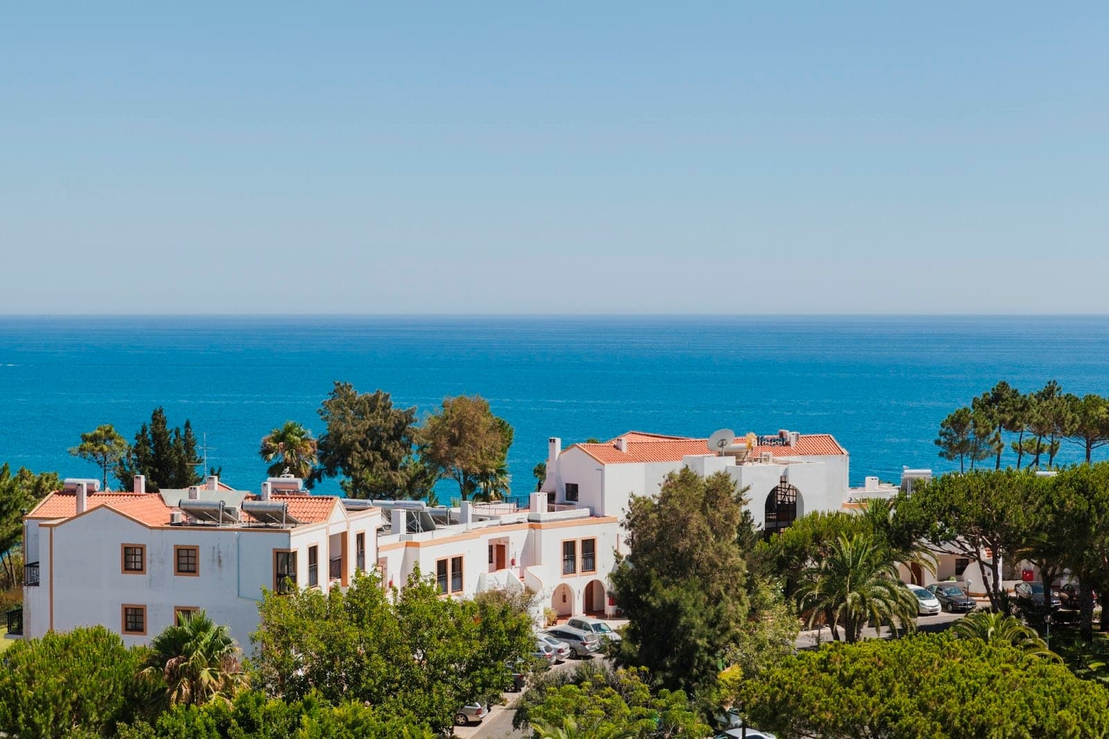 White buildings with terracotta roofs overlook a blue sea under a clear sky.