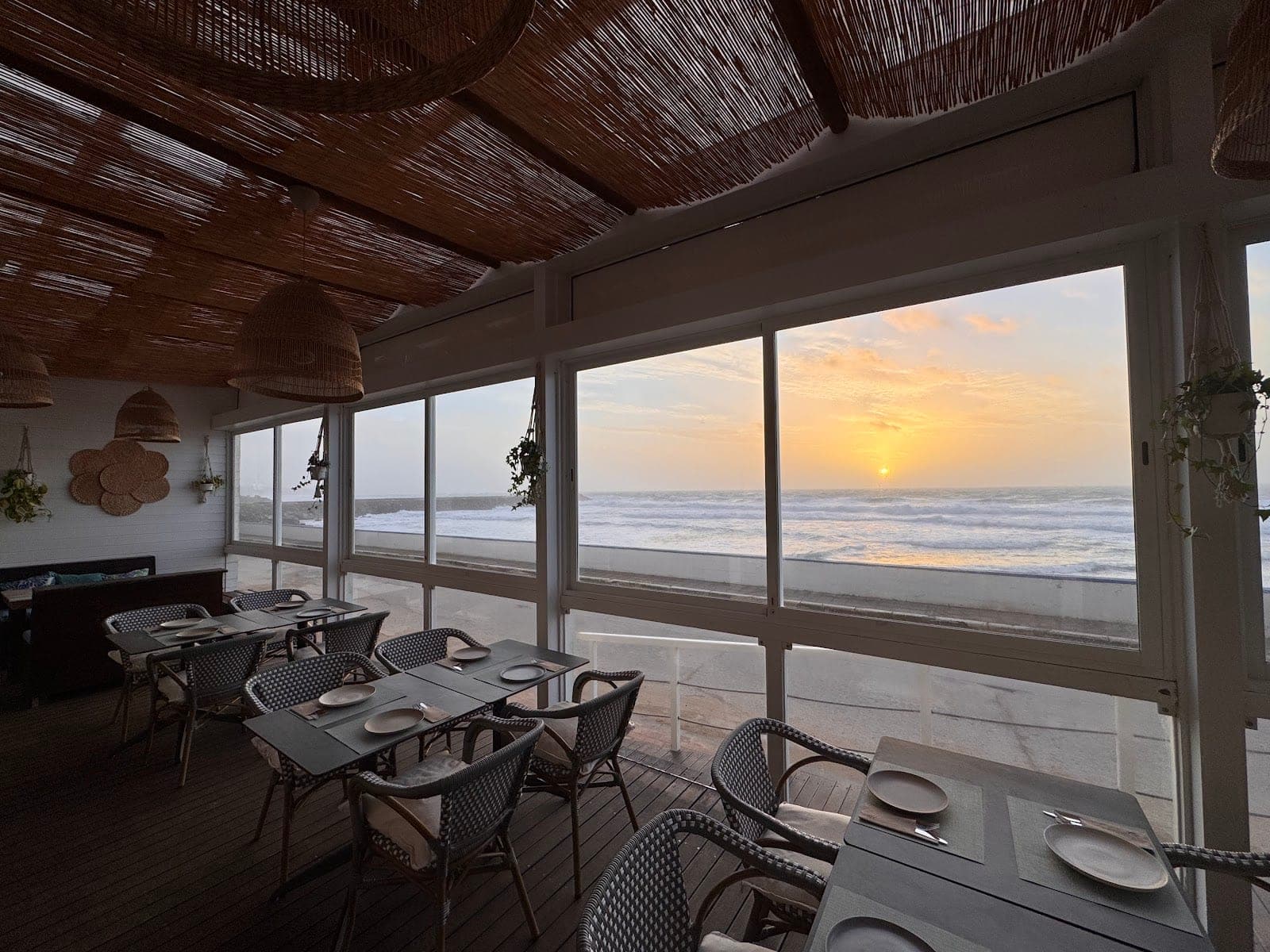 Restaurant dining room with tables set, overlooking the ocean at sunset.