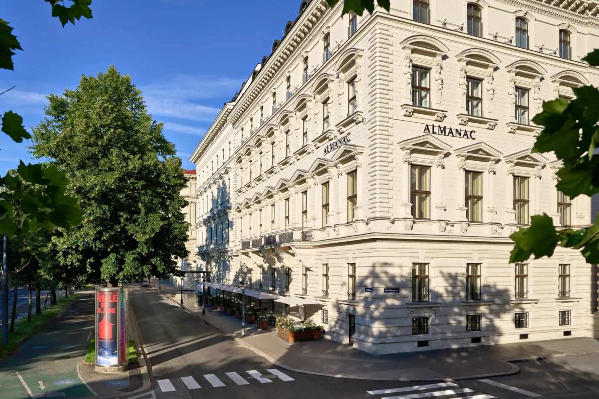 Exterior of the Almanac hotel building with trees and a street in front.