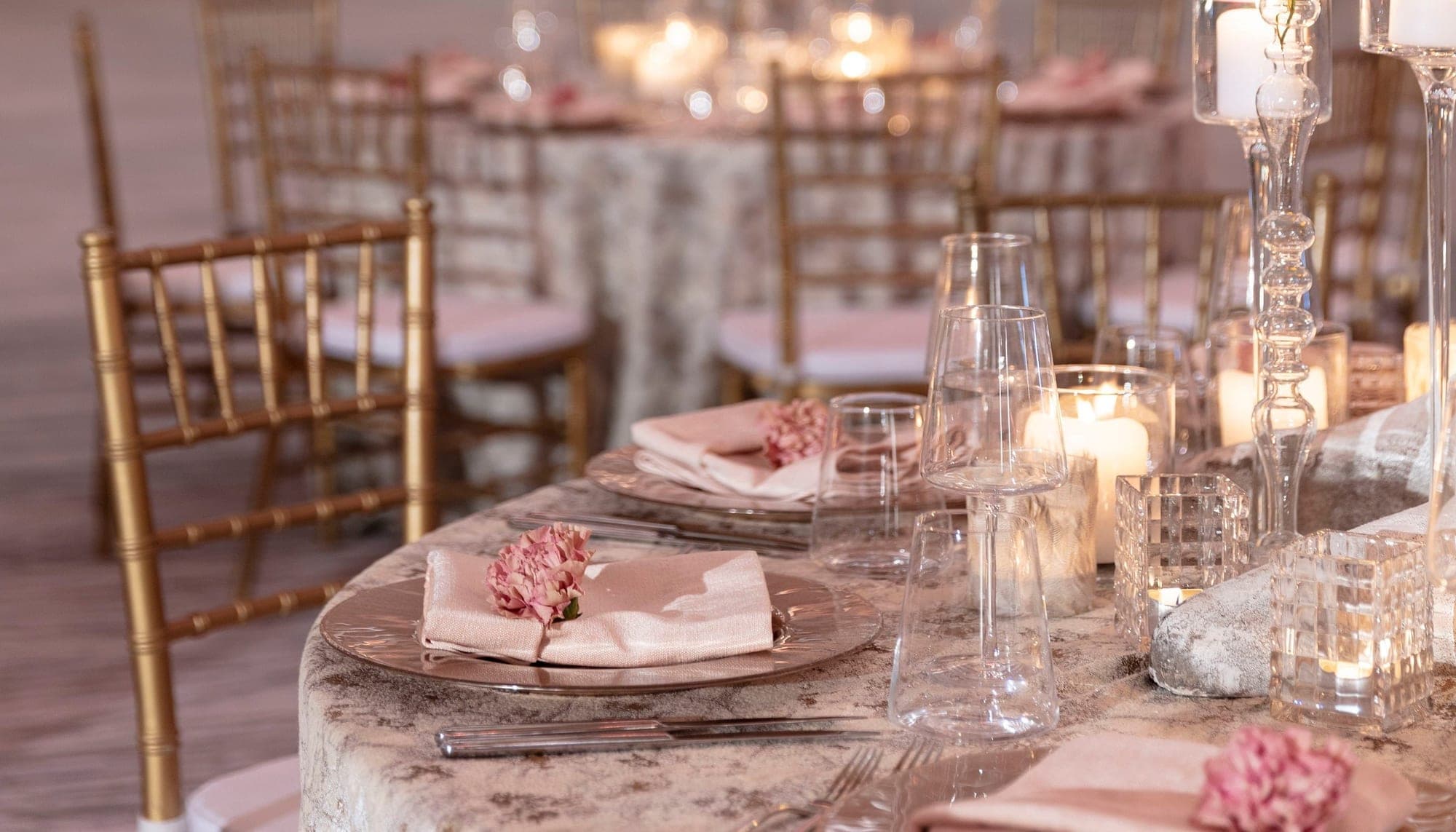A wedding reception table setting with gold chairs and pink floral details.