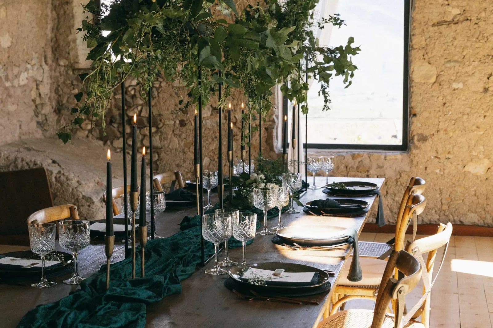 A long wooden table set for a wedding reception with dark plates and green velvet runner.
