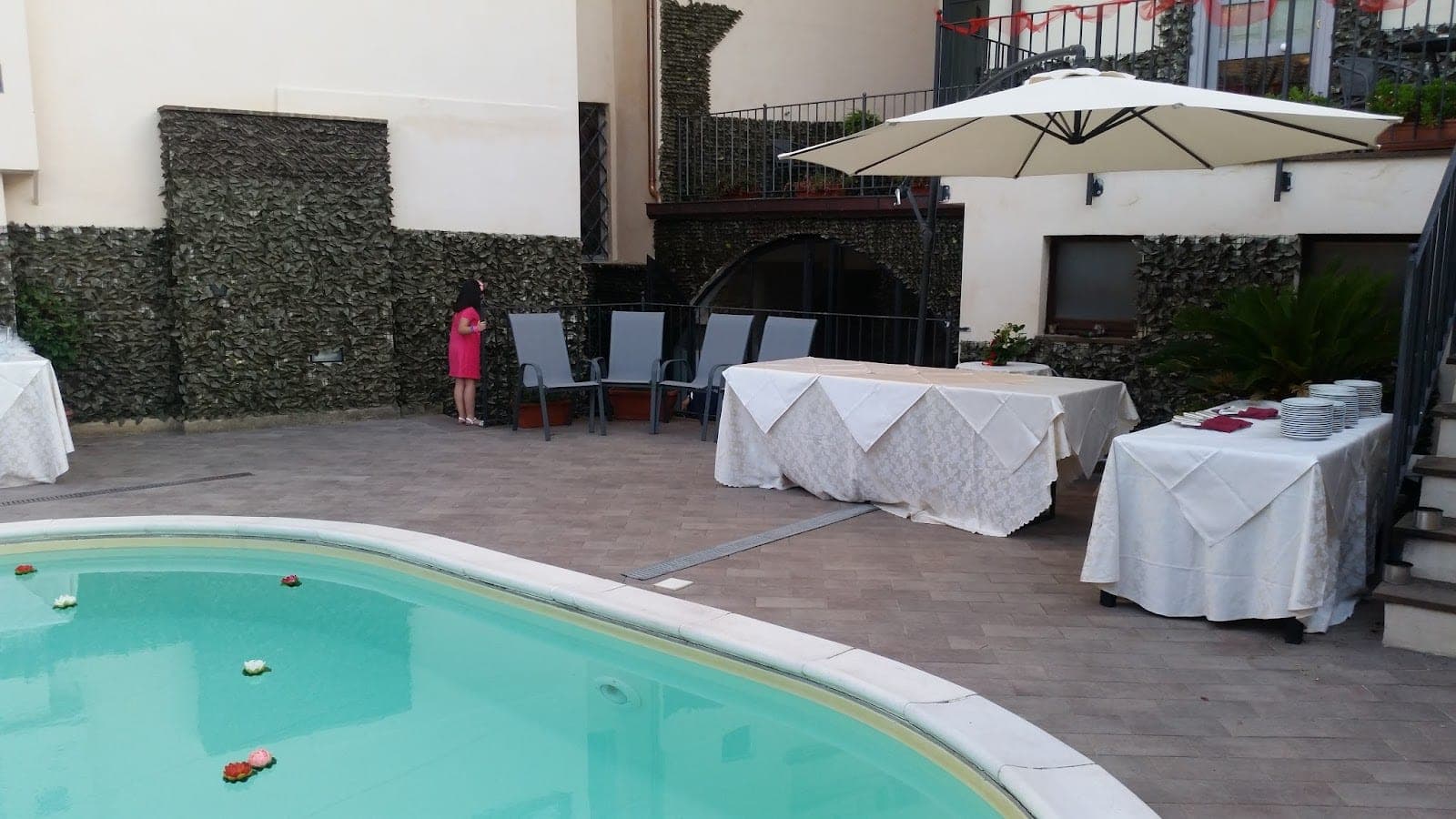 Courtyard with a pool, tables set for an event, and a person standing near chairs.