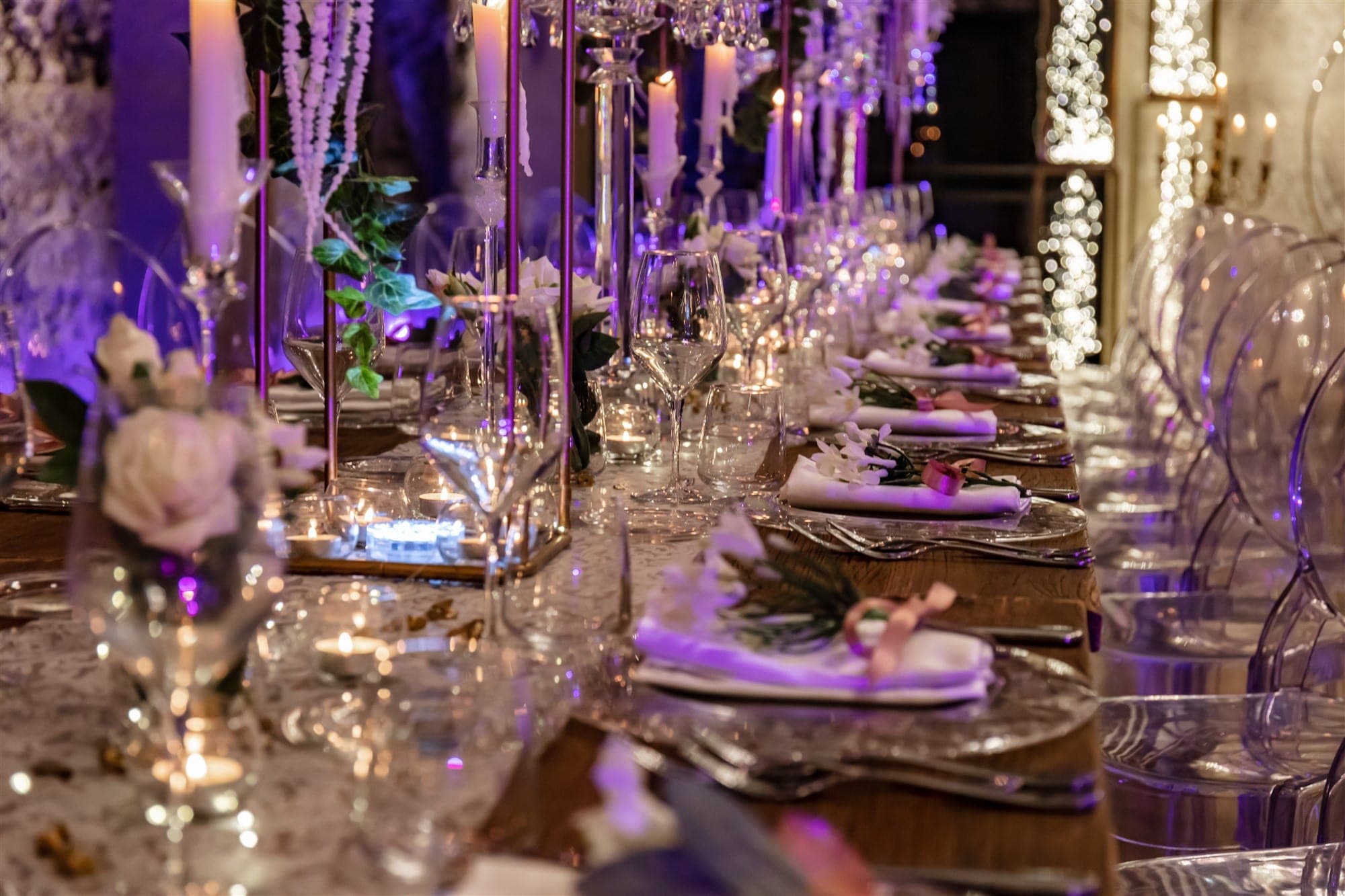 A long reception table is set with elegant place settings, candles, and floral arrangements.