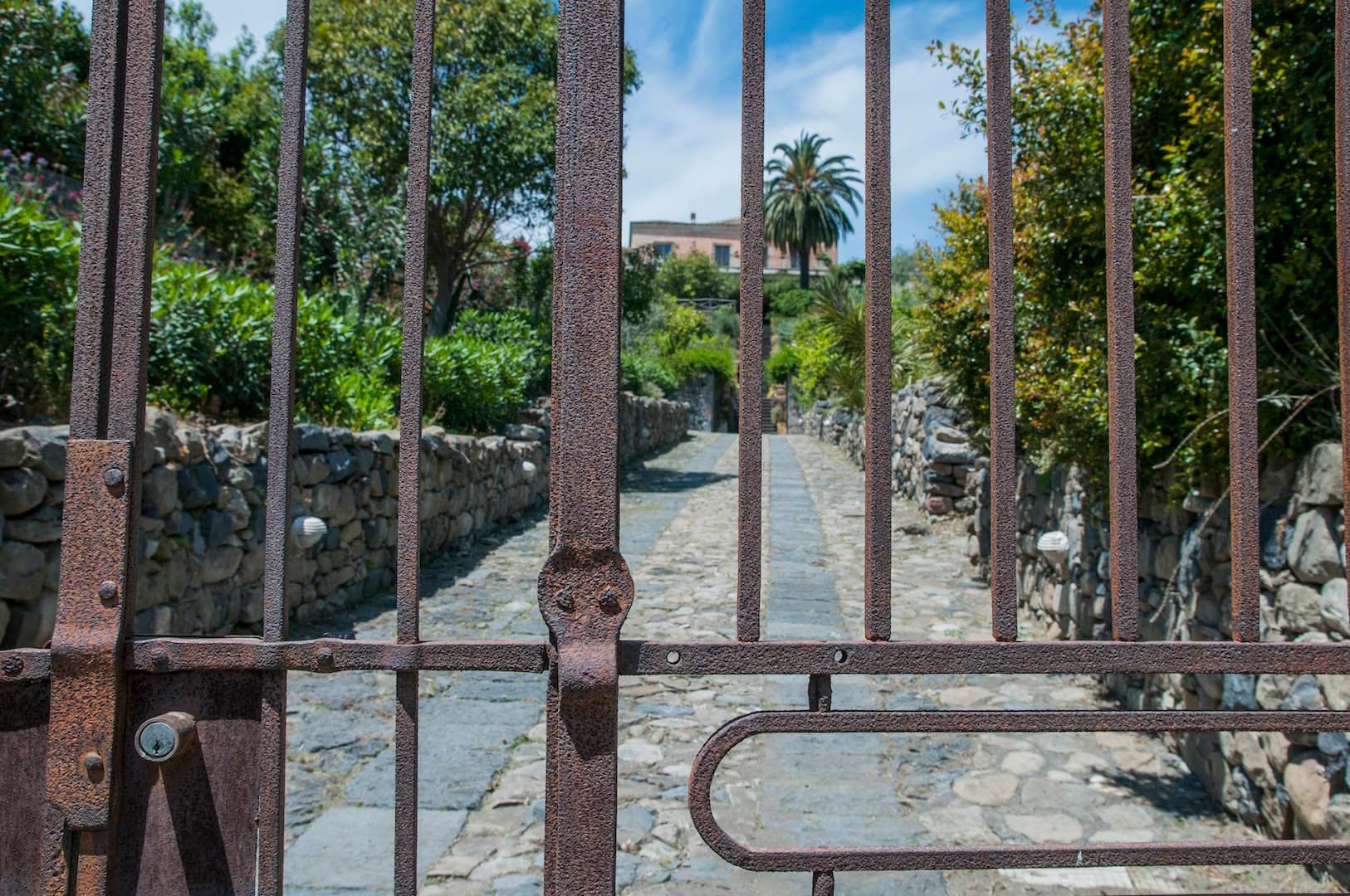 A pathway through a rusty gate towards a building at Antico Borgo Etneo Country Hotel.