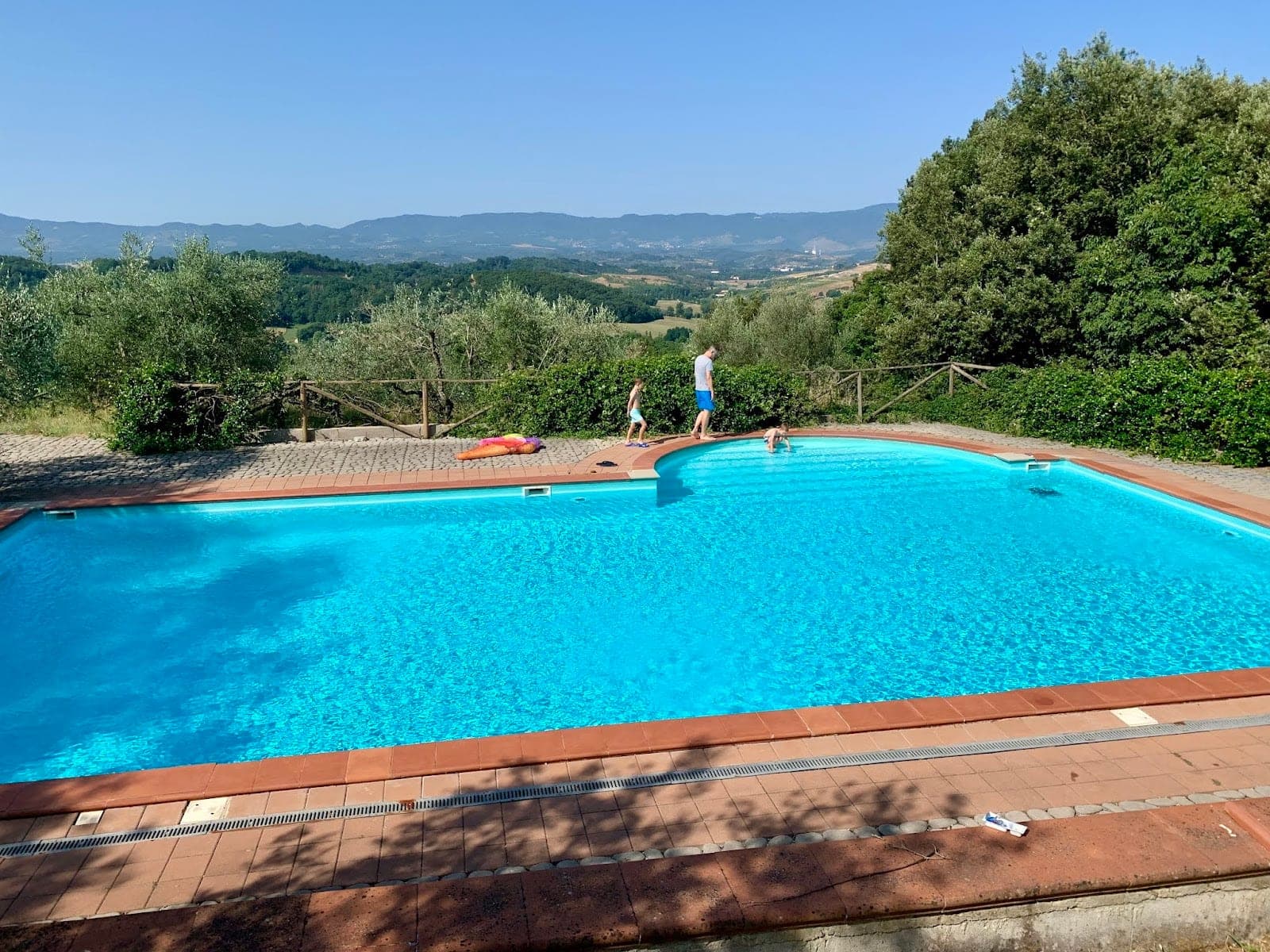 A swimming pool with a view of rolling hills and trees under a clear blue sky.