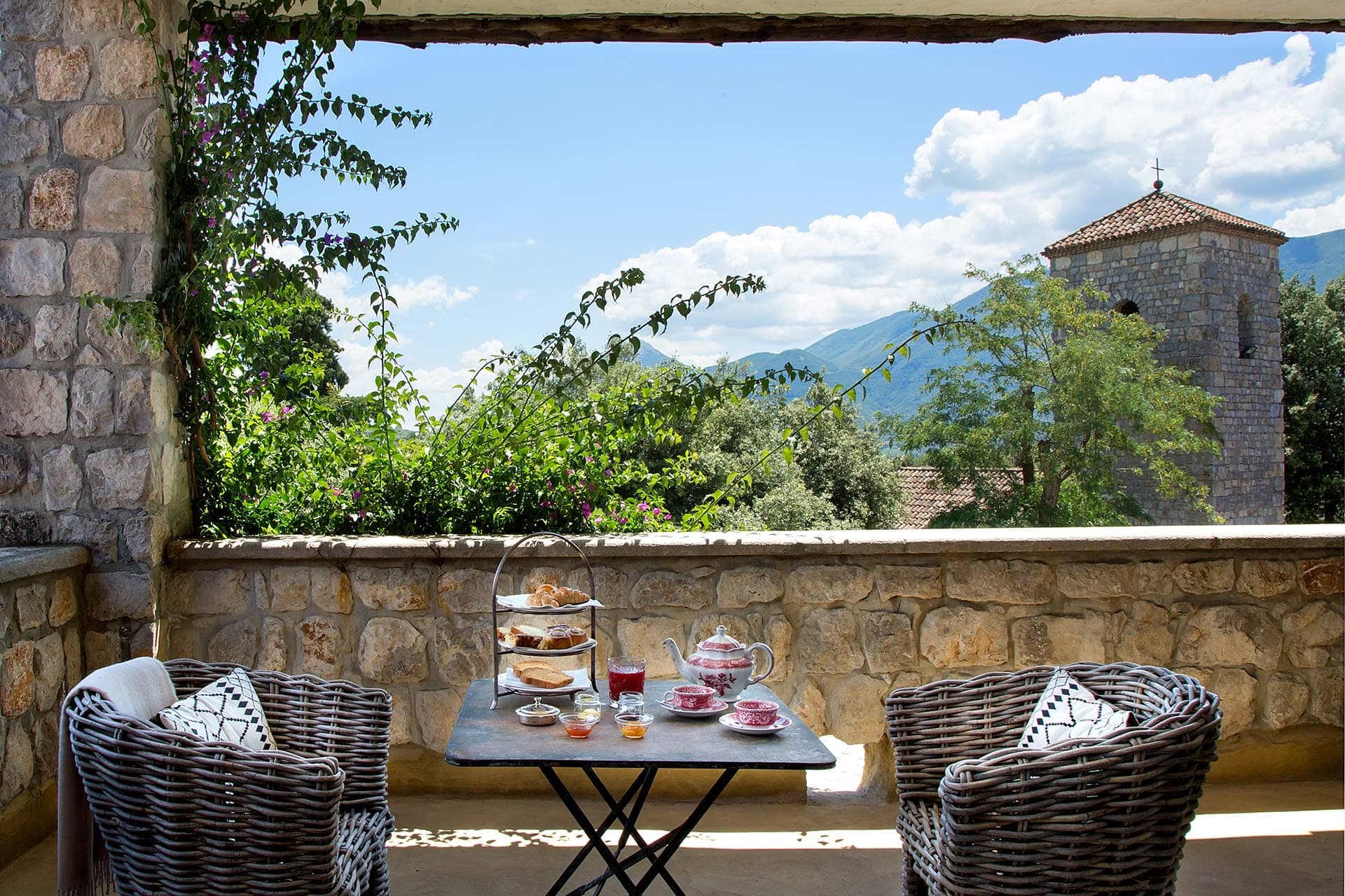 A table set for tea on a balcony overlooking a landscape with mountains and a tower.