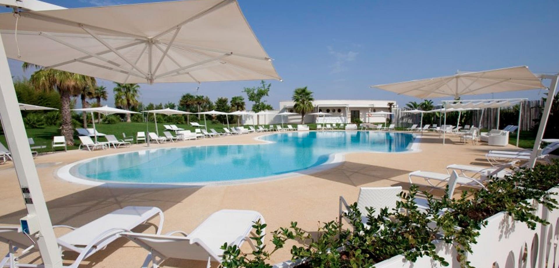 A large swimming pool with lounge chairs and umbrellas on a sunny day.