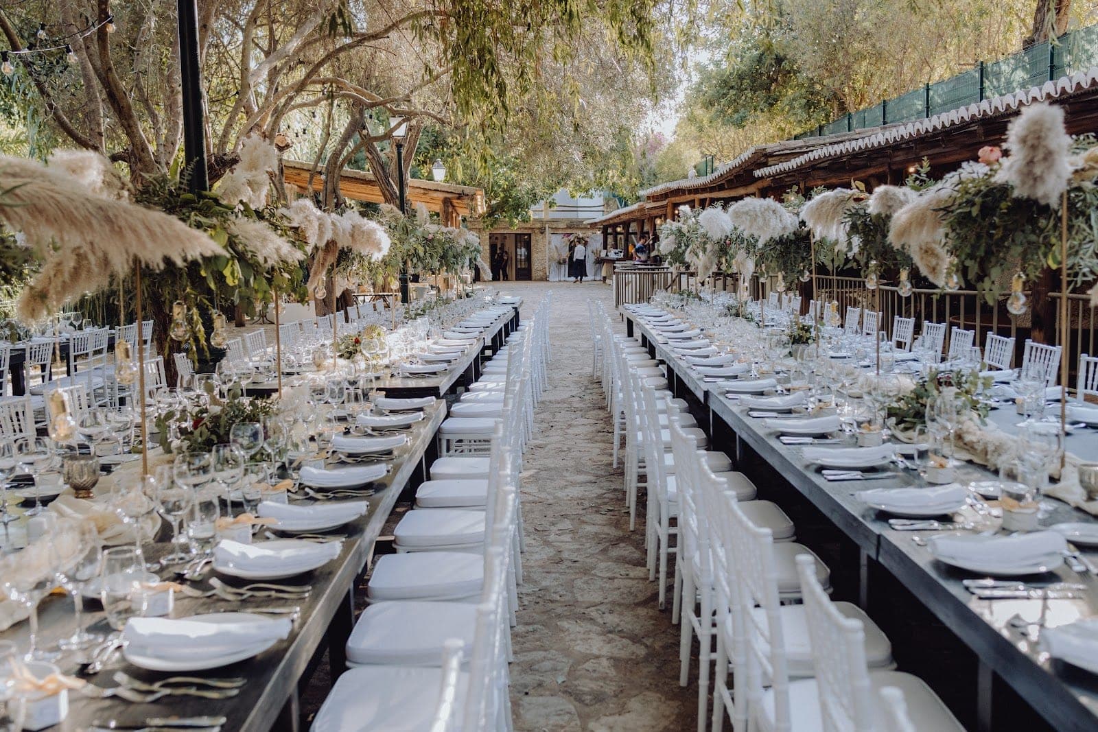 Long banquet tables set for an outdoor wedding reception with white chairs and floral decorations.