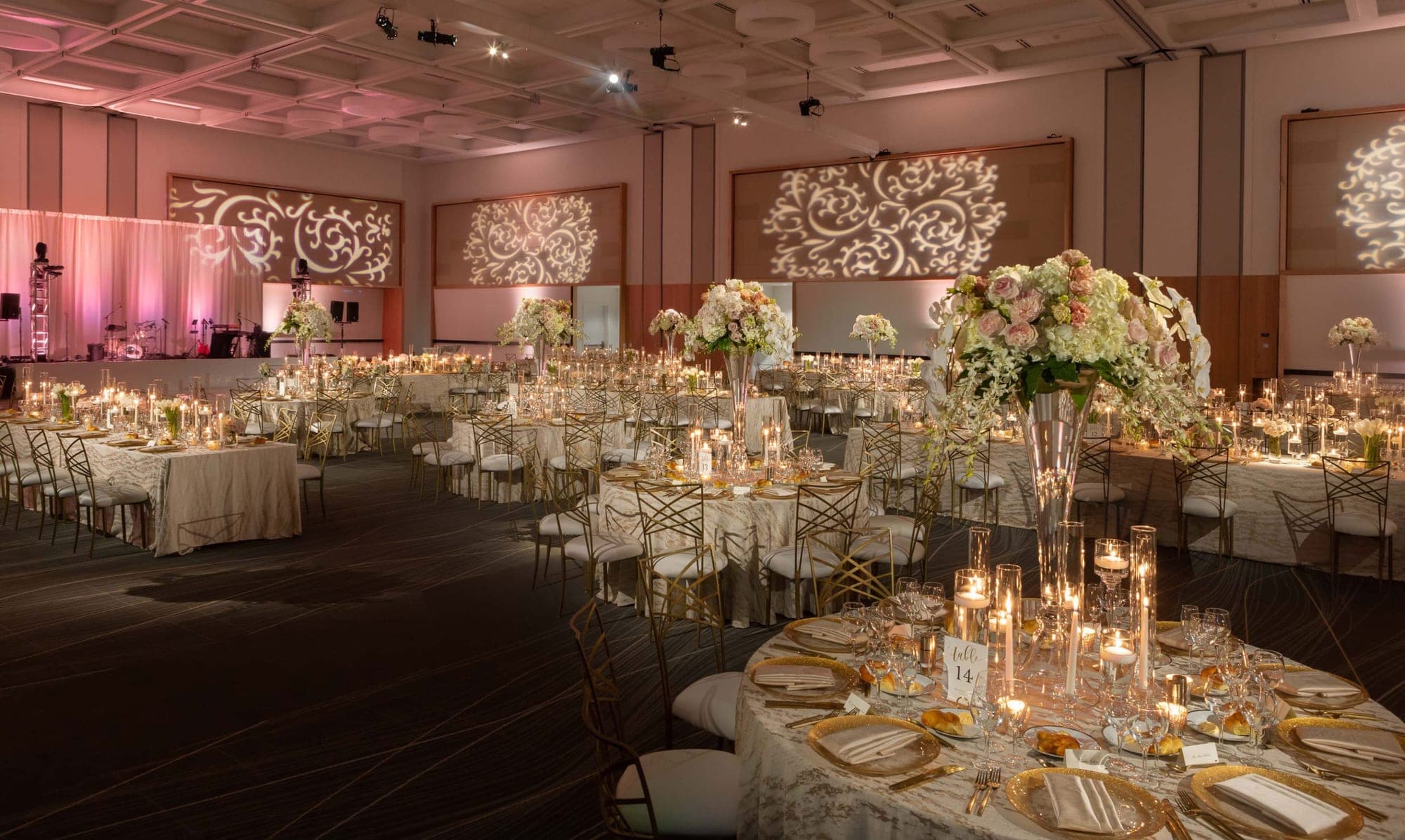 A reception hall set with many tables, chairs, and floral centerpieces.