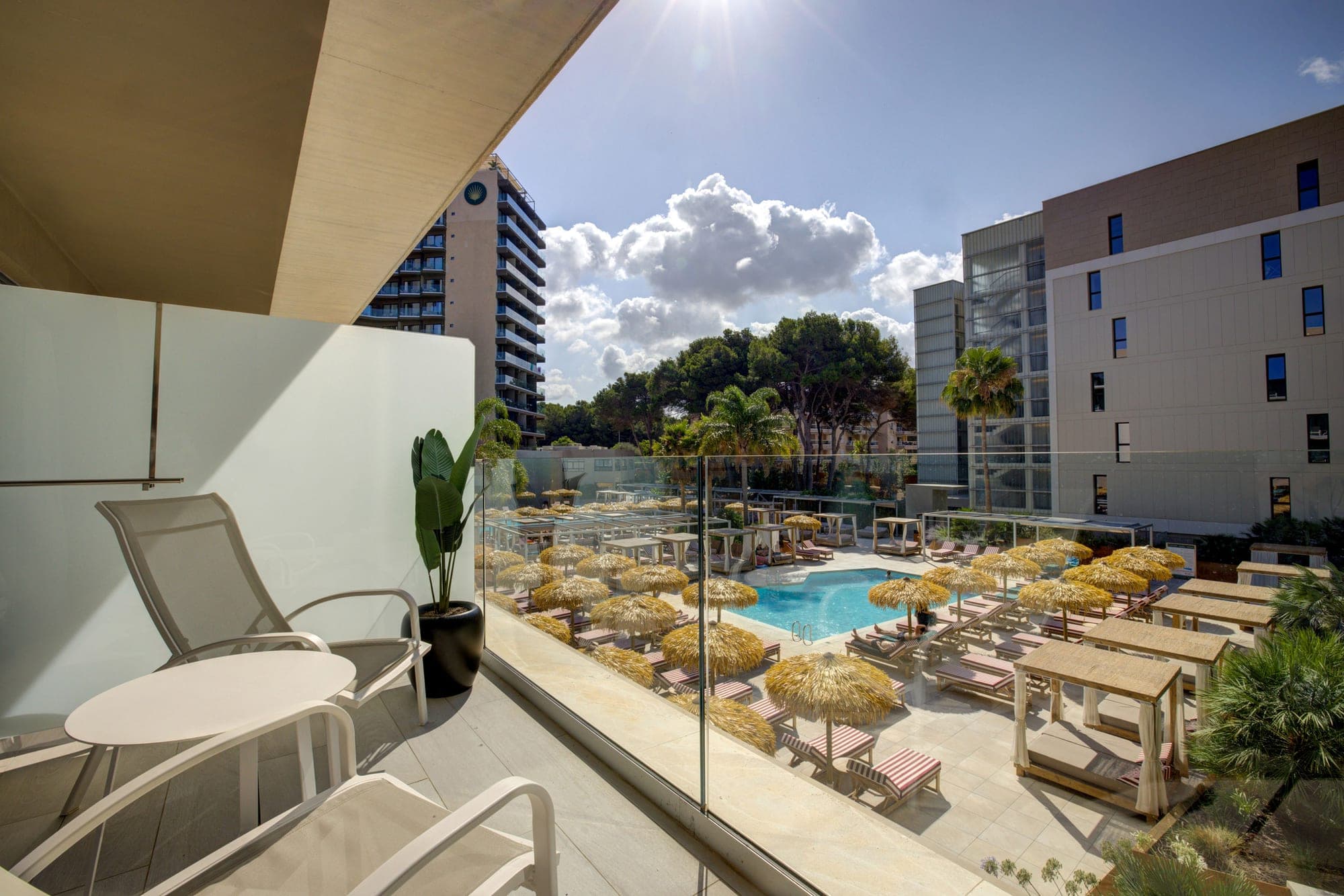 Resort pool area with sun loungers and umbrellas viewed from a balcony.