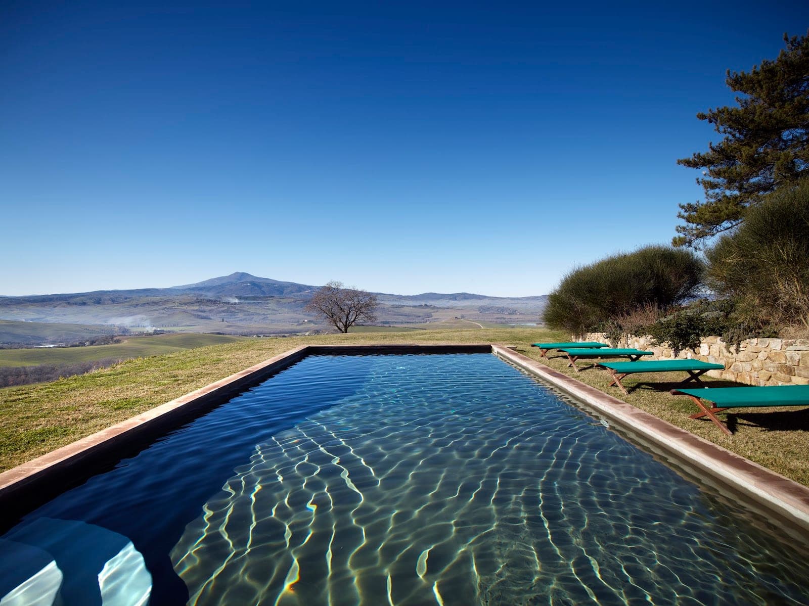 A swimming pool with loungers overlooks a rolling landscape under a clear blue sky.