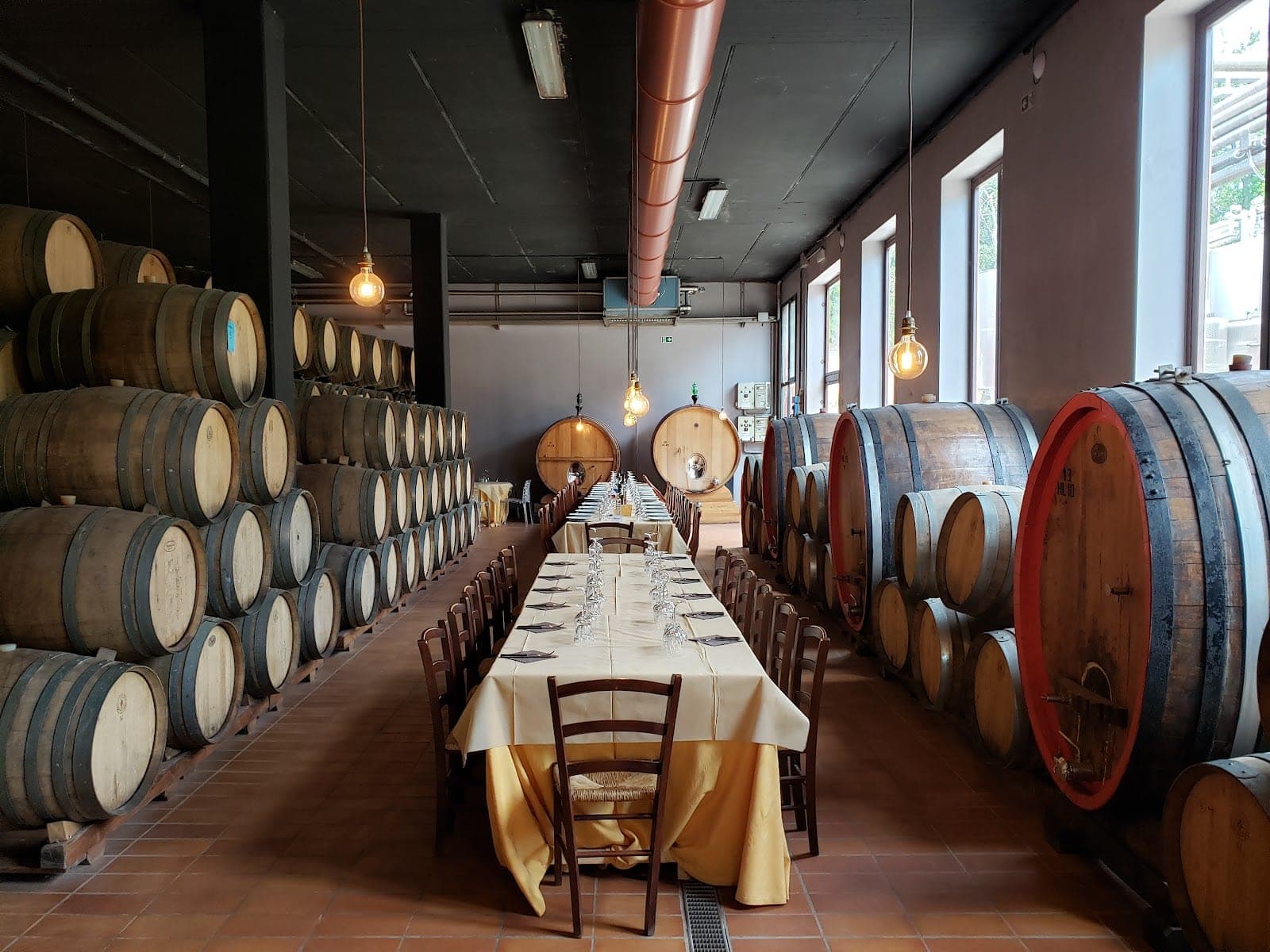 A long reception table is set up in a wine cellar with many wooden barrels.
