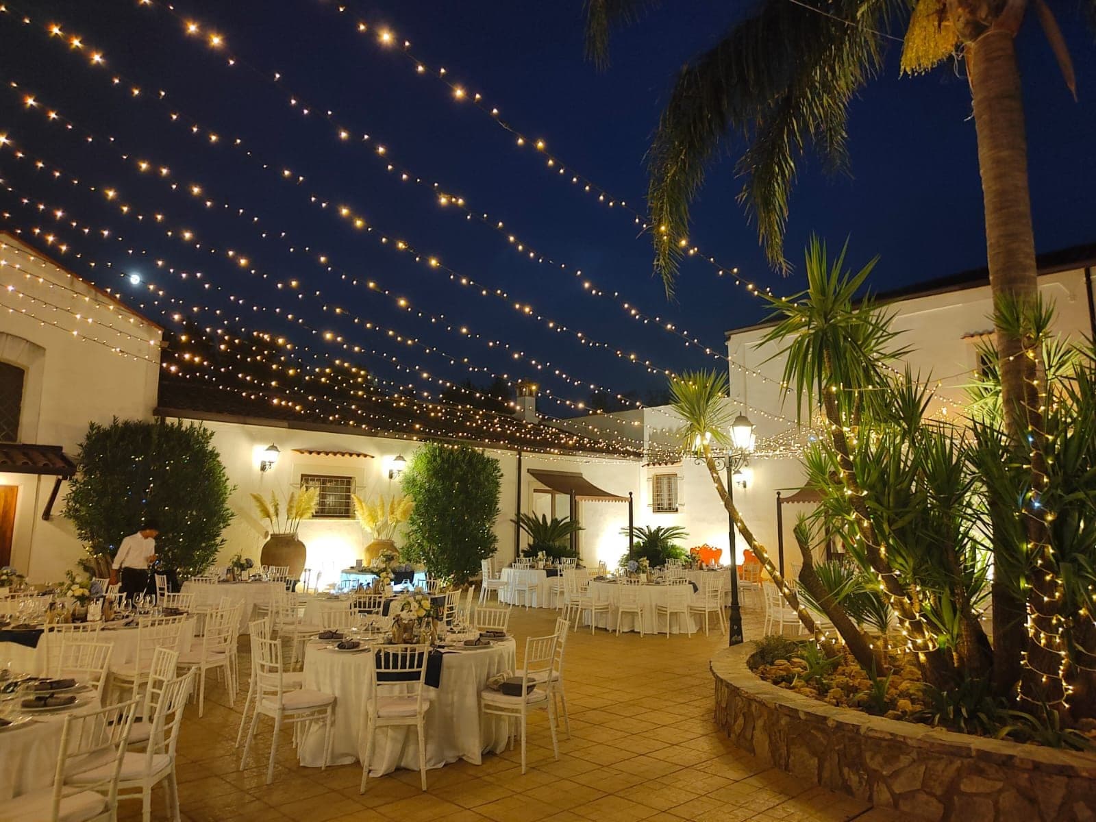 Courtyard reception area with tables, chairs, and fairy lights at night.