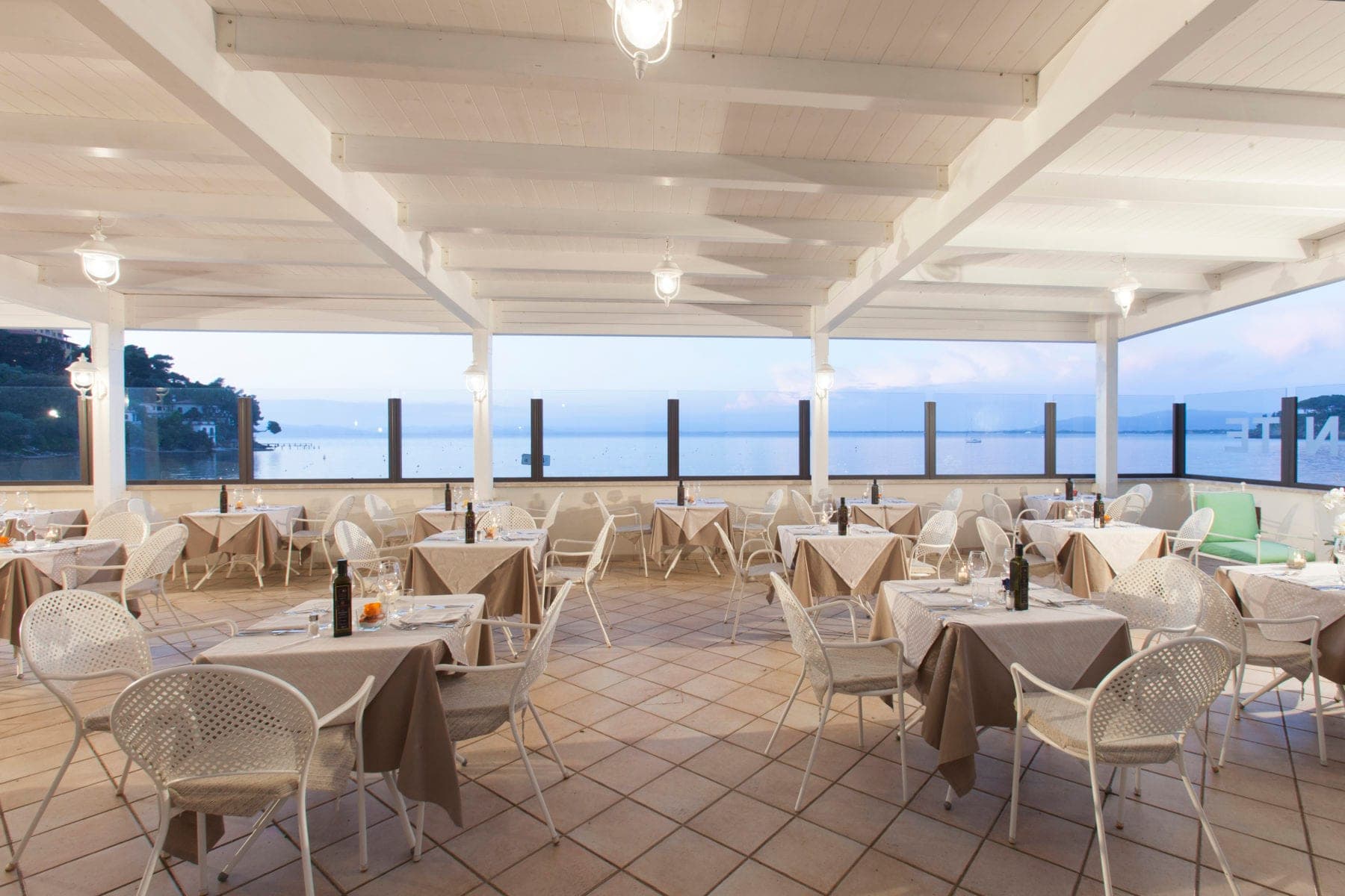 Covered outdoor dining area with tables set for a meal, overlooking the sea.