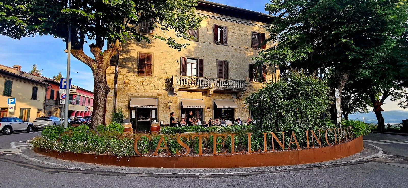 Exterior of a building with outdoor seating and a large metal sign that says Castellina in Chianti.