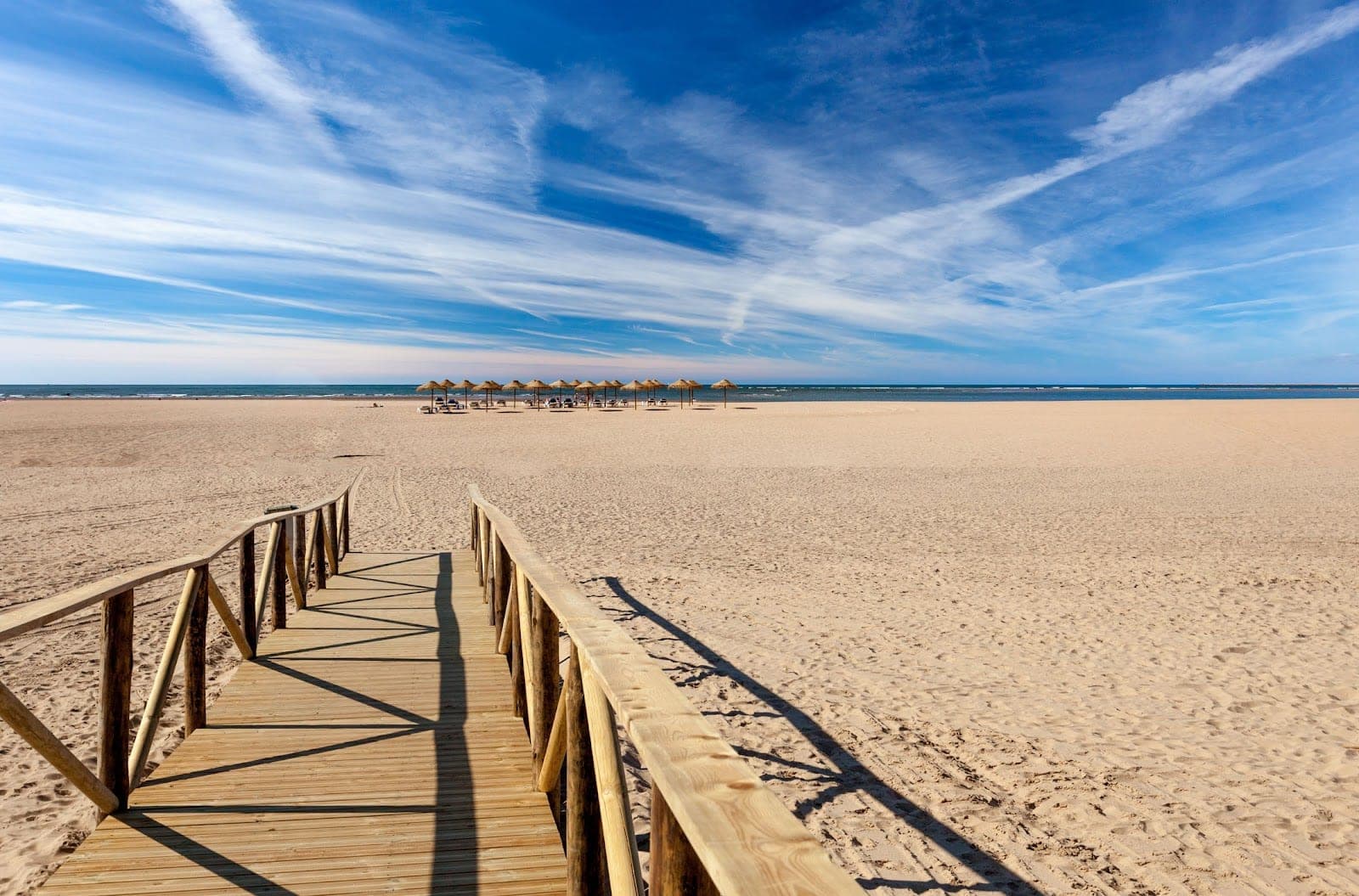 Wooden walkway on a sandy beach with umbrellas and the sea.