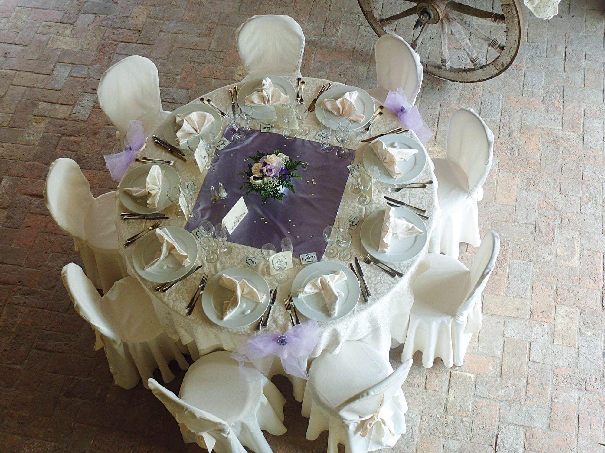 A round table is set for a wedding reception with white chairs and floral centerpieces.