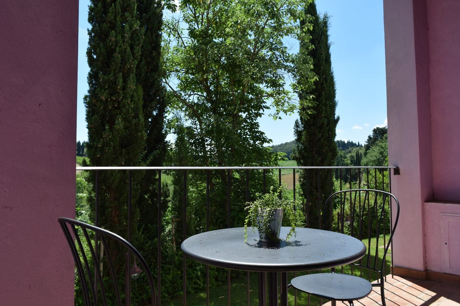 A table and chairs on a balcony overlooking a garden with cypress trees.