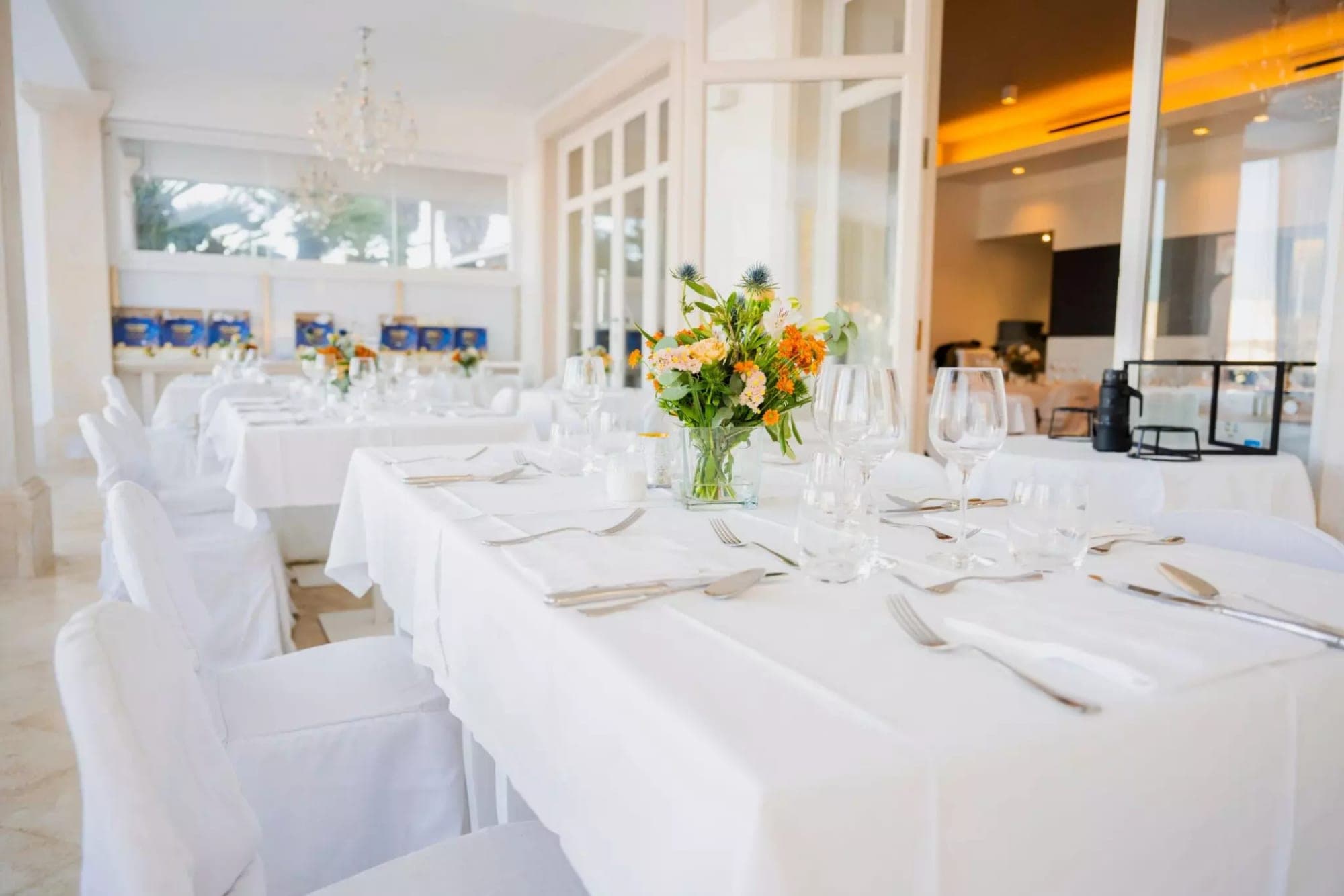 A reception table is set with white linens, glassware, and floral centerpieces.