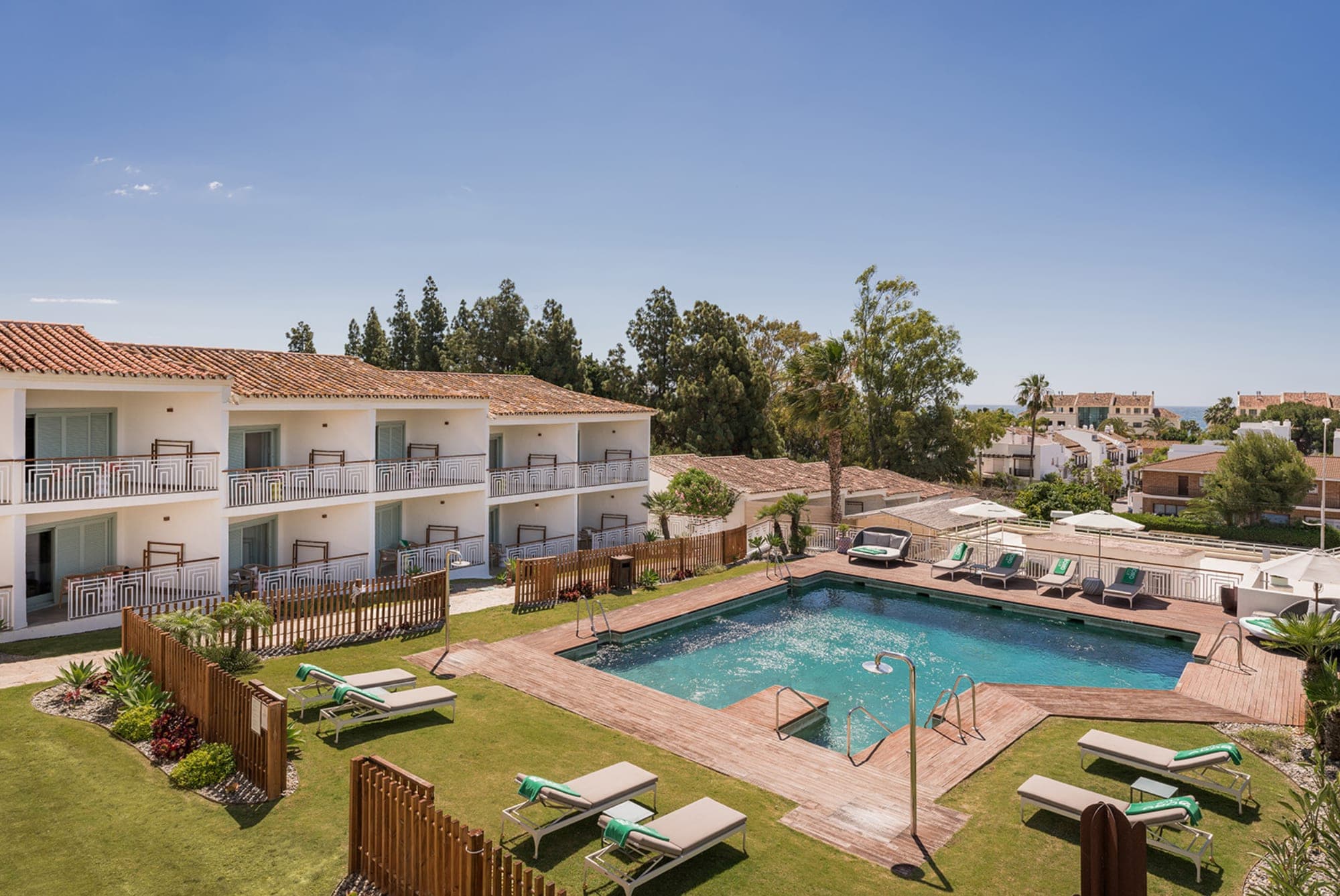 Hotel rooms and swimming pool area with lounge chairs and umbrellas.