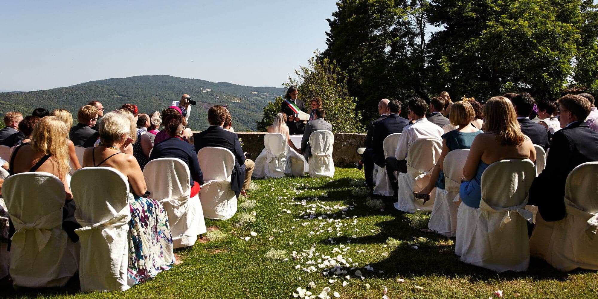 Outdoor wedding ceremony with guests seated and a scenic view of hills.