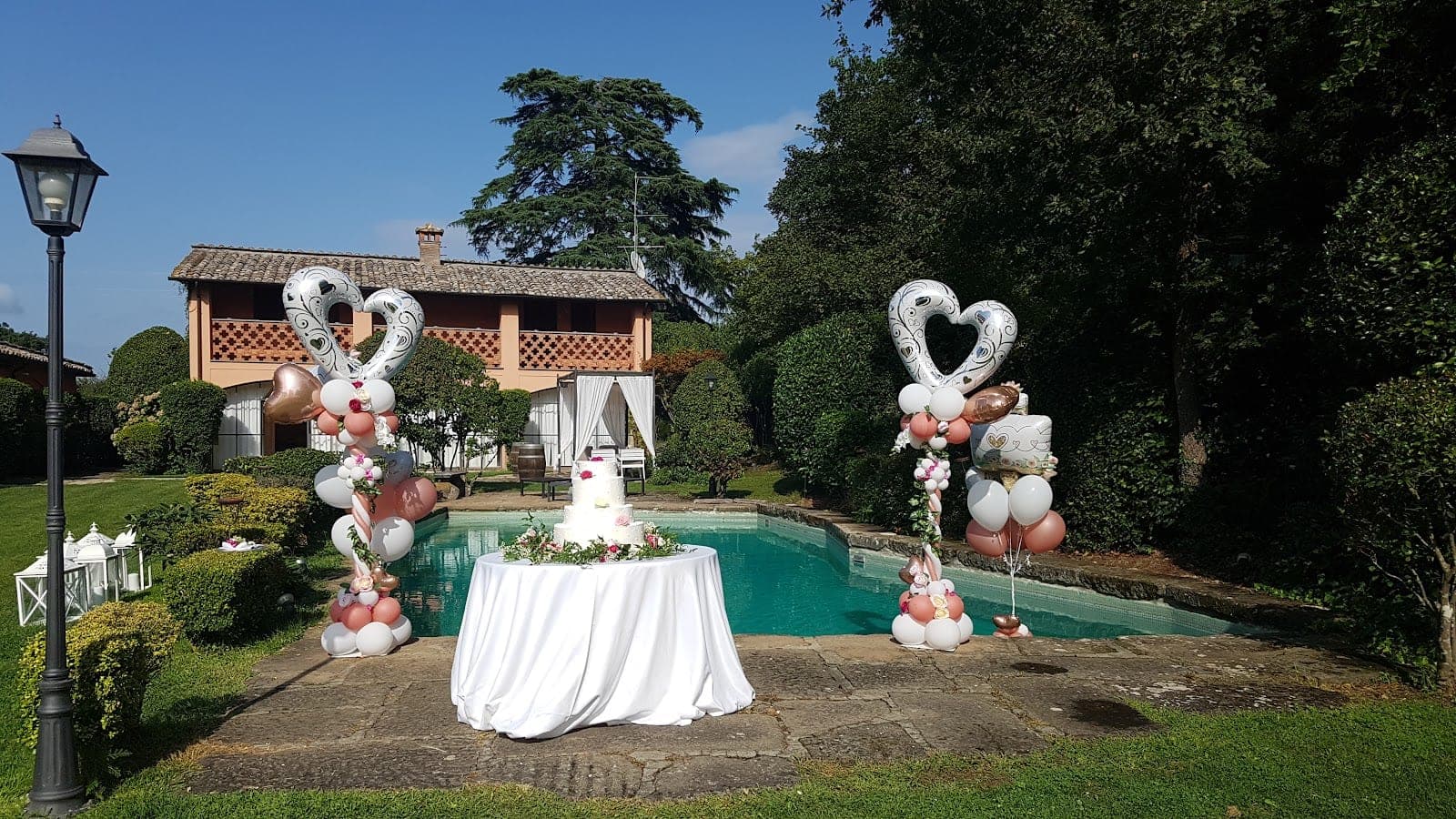 Wedding cake and balloons by a swimming pool at a venue.