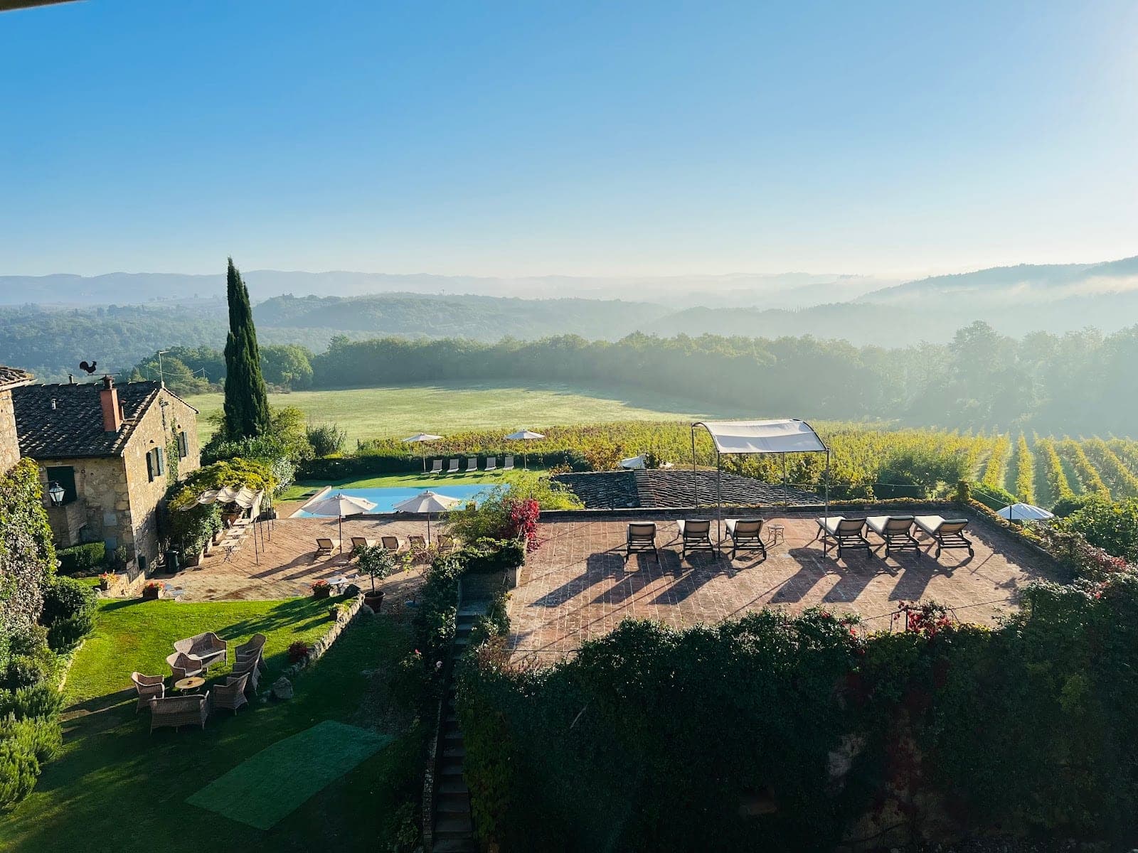 View of a Tuscan villa with vineyards, a swimming pool, and rolling hills in the background.