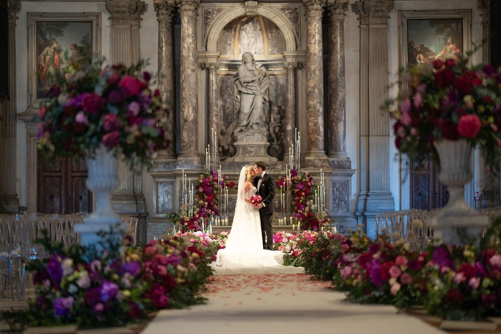 A bride and groom kiss in front of an altar decorated with flowers and candles.