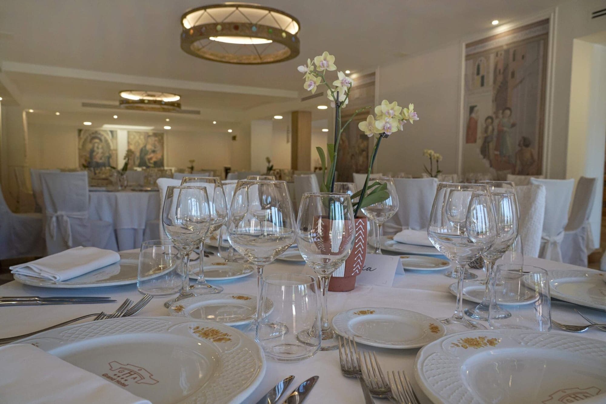 A table set for a wedding reception with white tablecloths, plates, glasses, and a floral centerpiece.