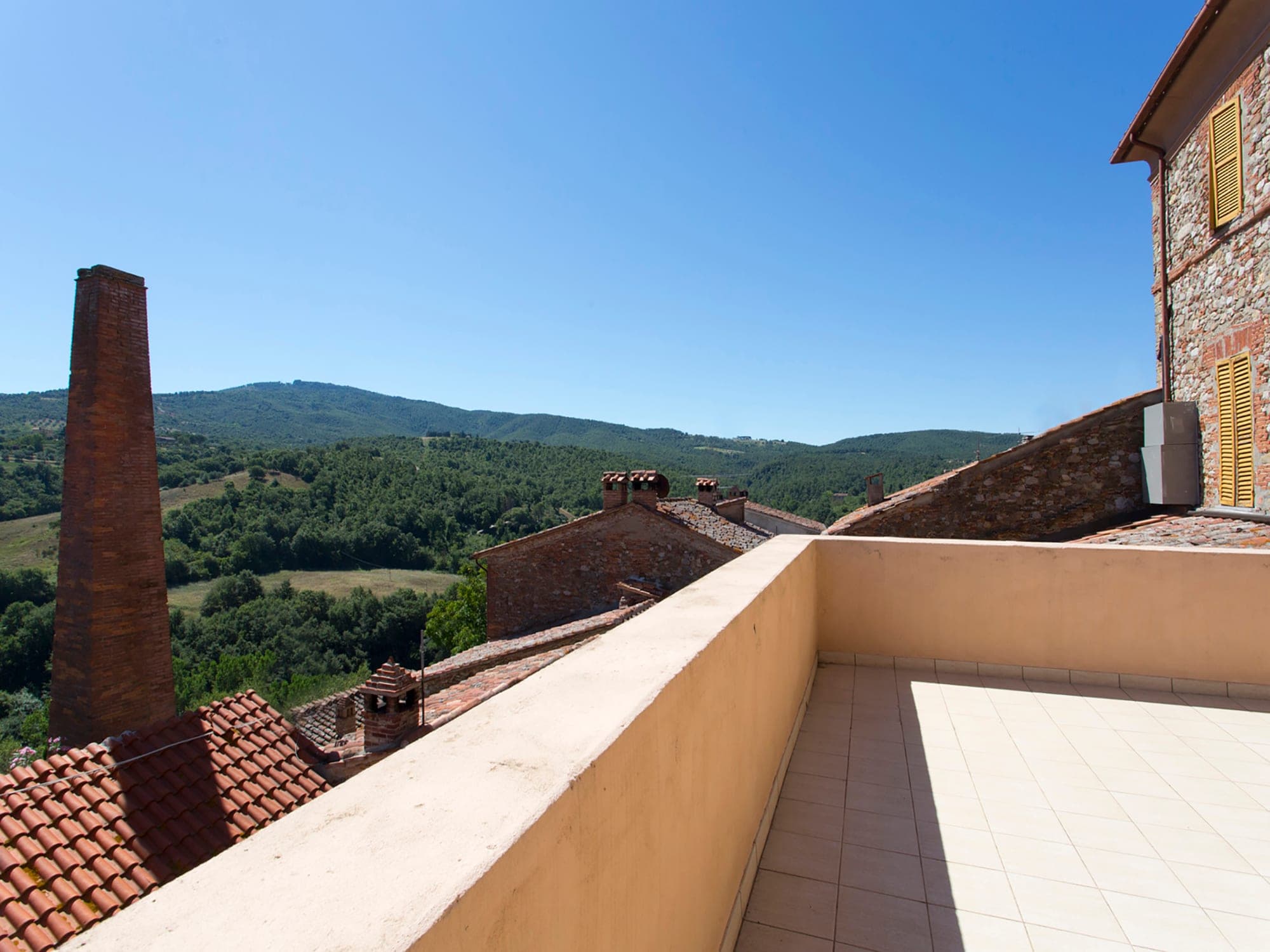 Terrace overlooking rooftops and green hills under a clear blue sky.