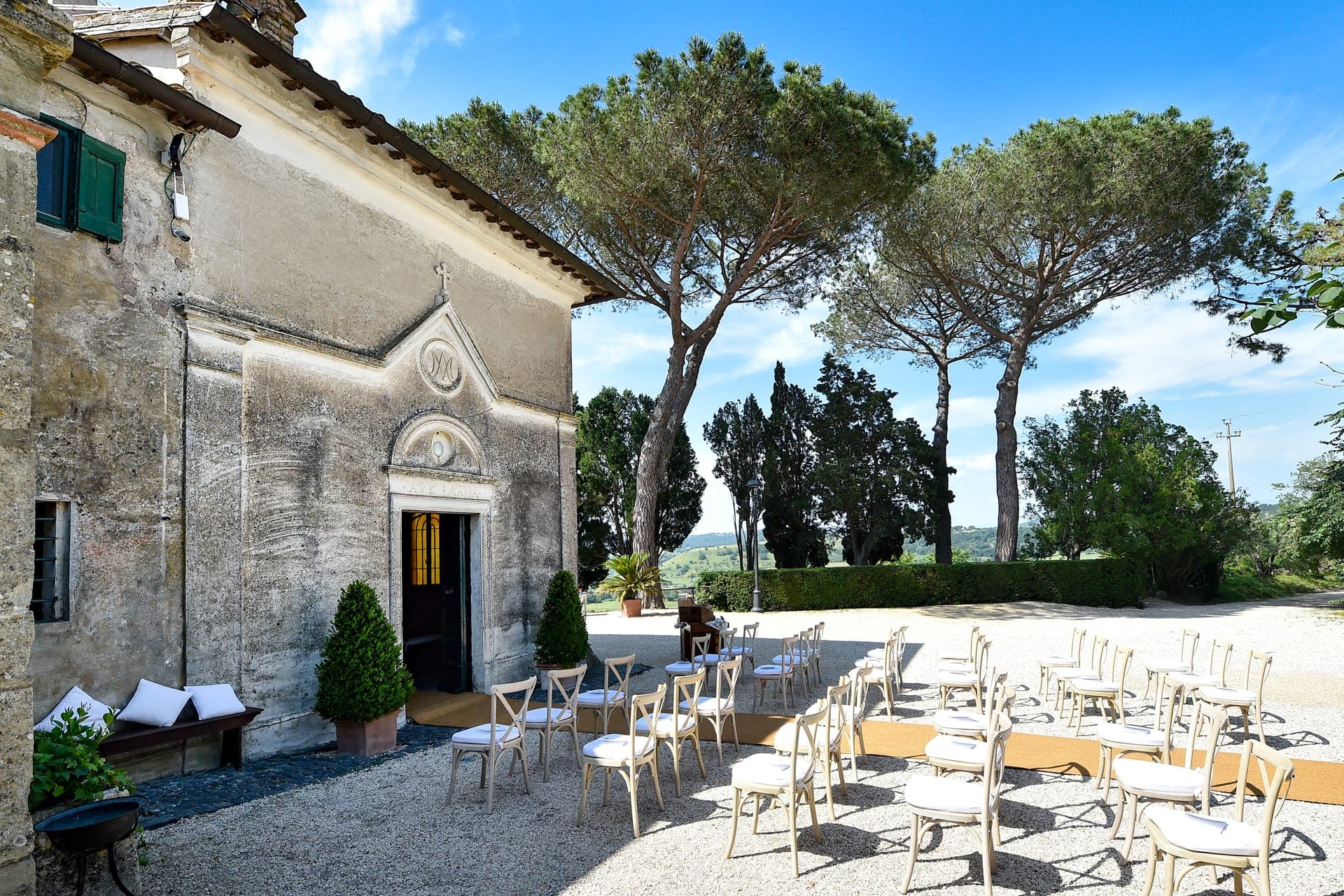 Outdoor wedding ceremony setup with chairs facing a building and trees.